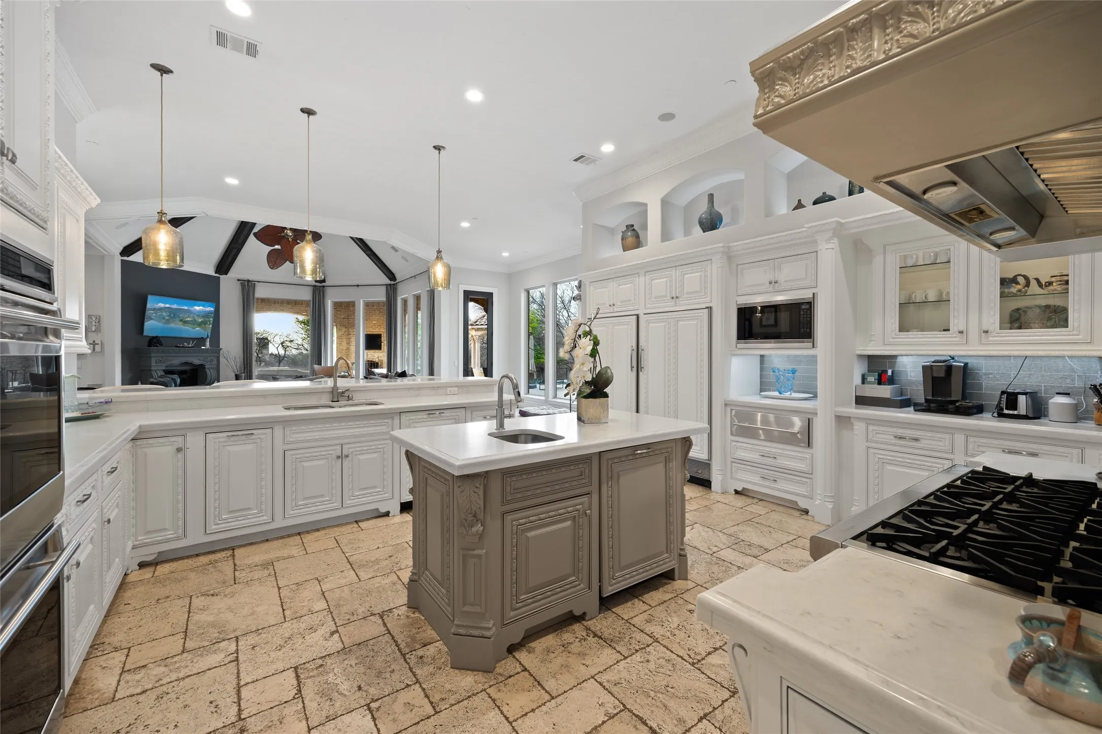 Gourmet kitchen featuring stone tile flooring, a large center island with a sink, white cabinetry, integrated appliances, and recessed lighting