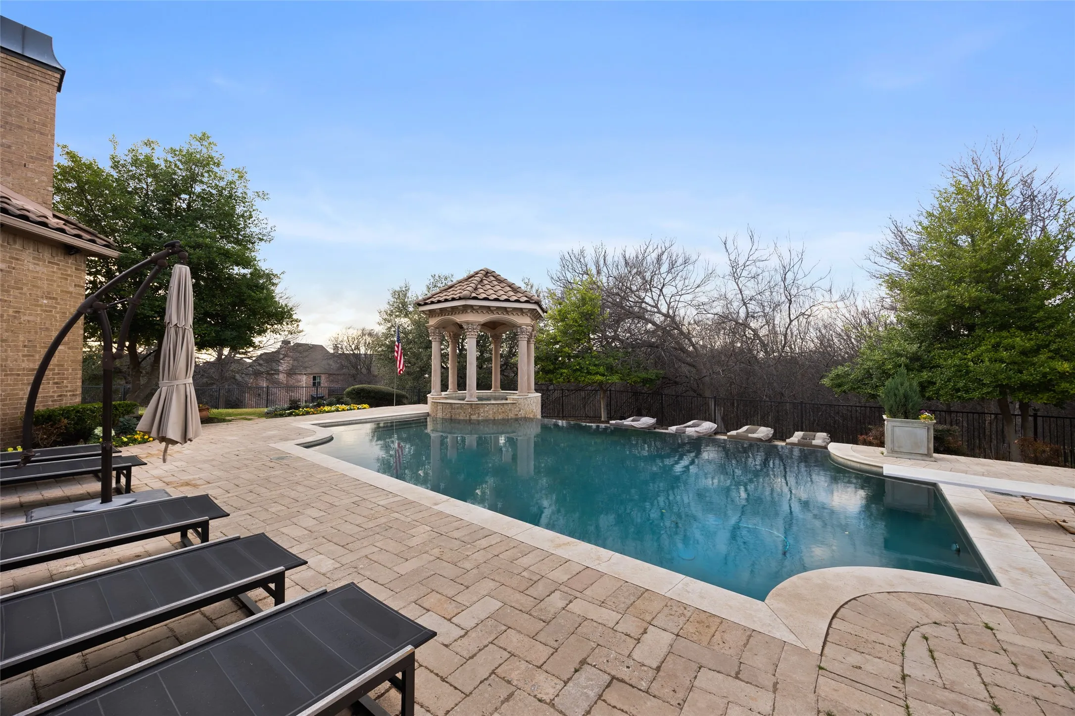 Resort-style pool with integrated gazebo, expansive paver patio, and stone coping
