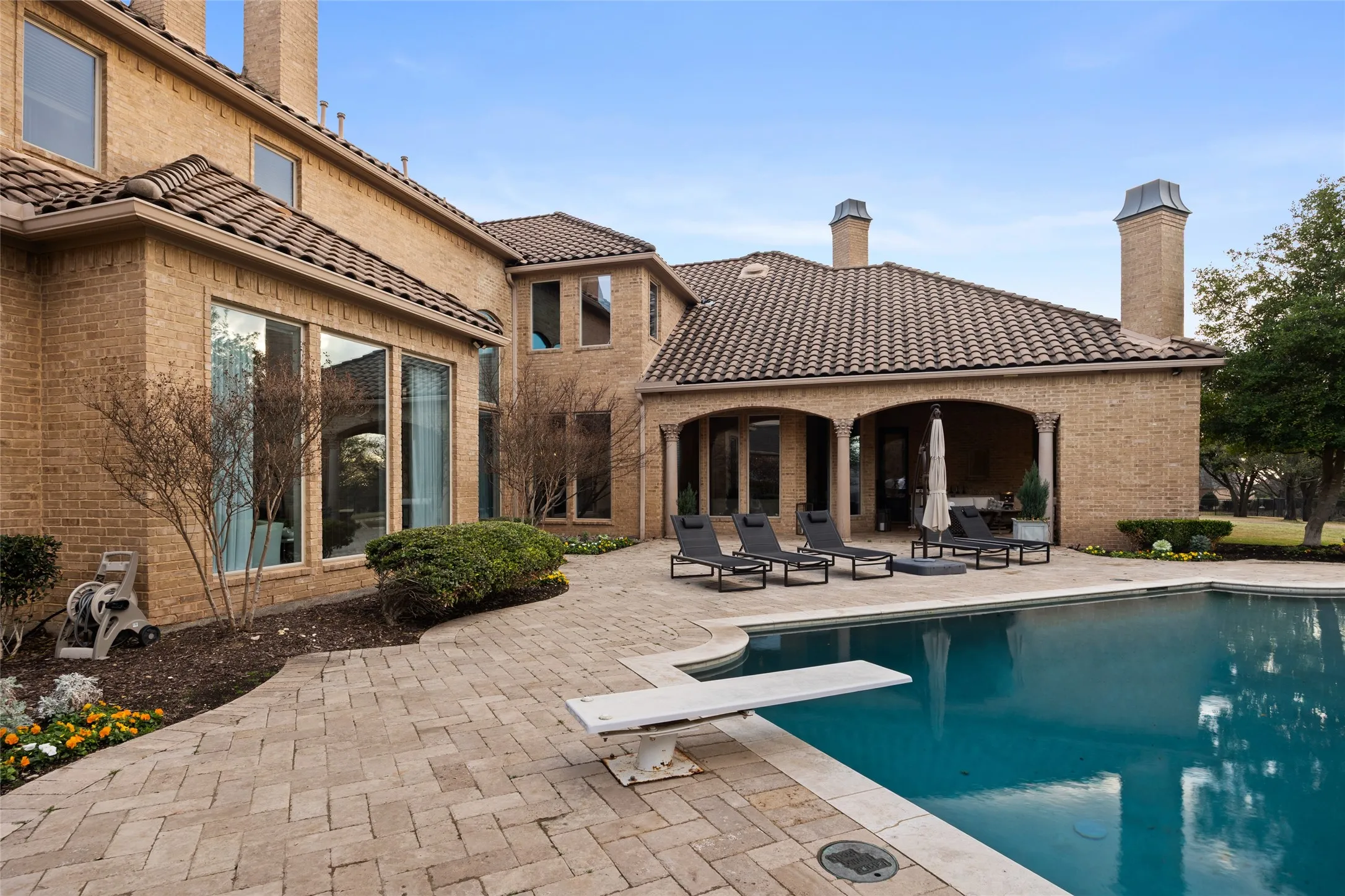 Brick exterior with arched covered patio, expansive pool with diving board, and paver patio