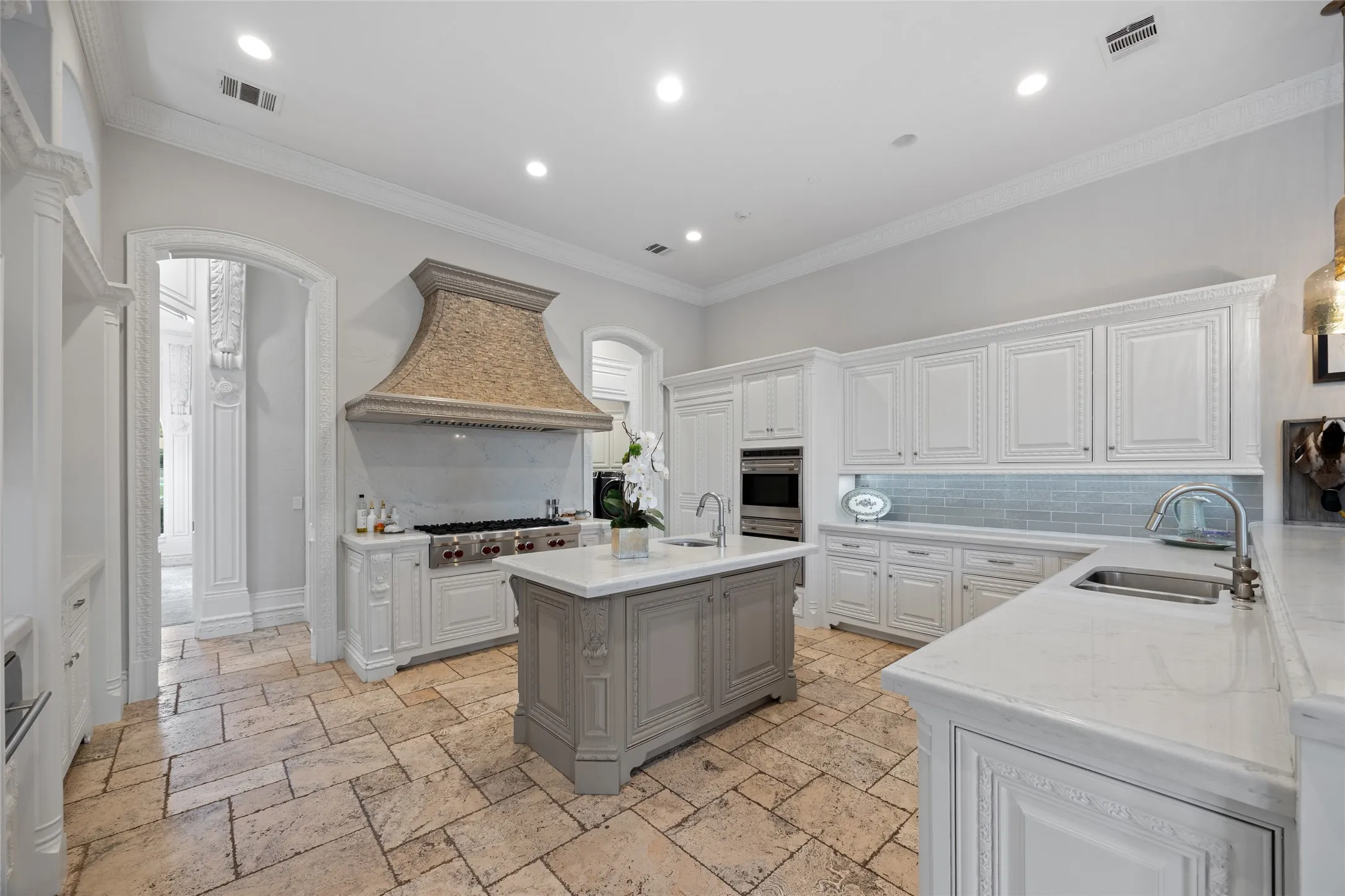 Kitchen featuring an oversized range hood, stainless steel appliances, a large center island, extensive cabinetry, and stone flooring