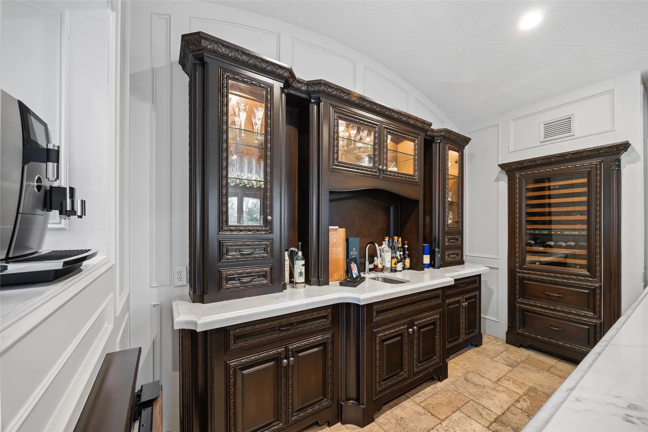 Built-in cabinetry with ornate detailing, glass-front upper cabinets with interior lighting, a built-in beverage refrigerator, a countertop with an integrated sink, and textured flooring