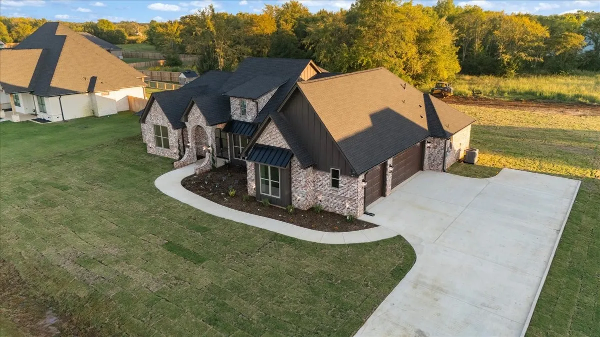 Exterior showcasing a brick and siding facade, arched entryway, dark shingles, an attached garage with wood-finish doors, and a concrete driveway