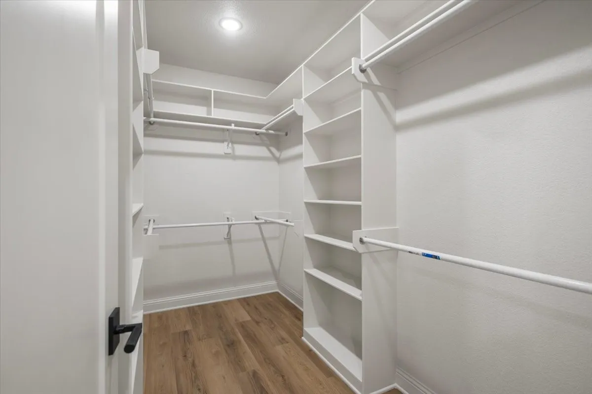 Walk-in closet featuring built-in shelving, multiple hanging rods, recessed lighting, and wood-finish flooring