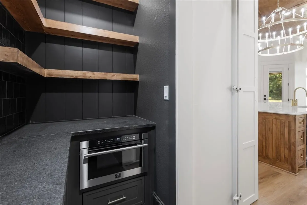 Built-in stainless steel microwave, dark countertop, open wood-finish shelving, and white paneled doors