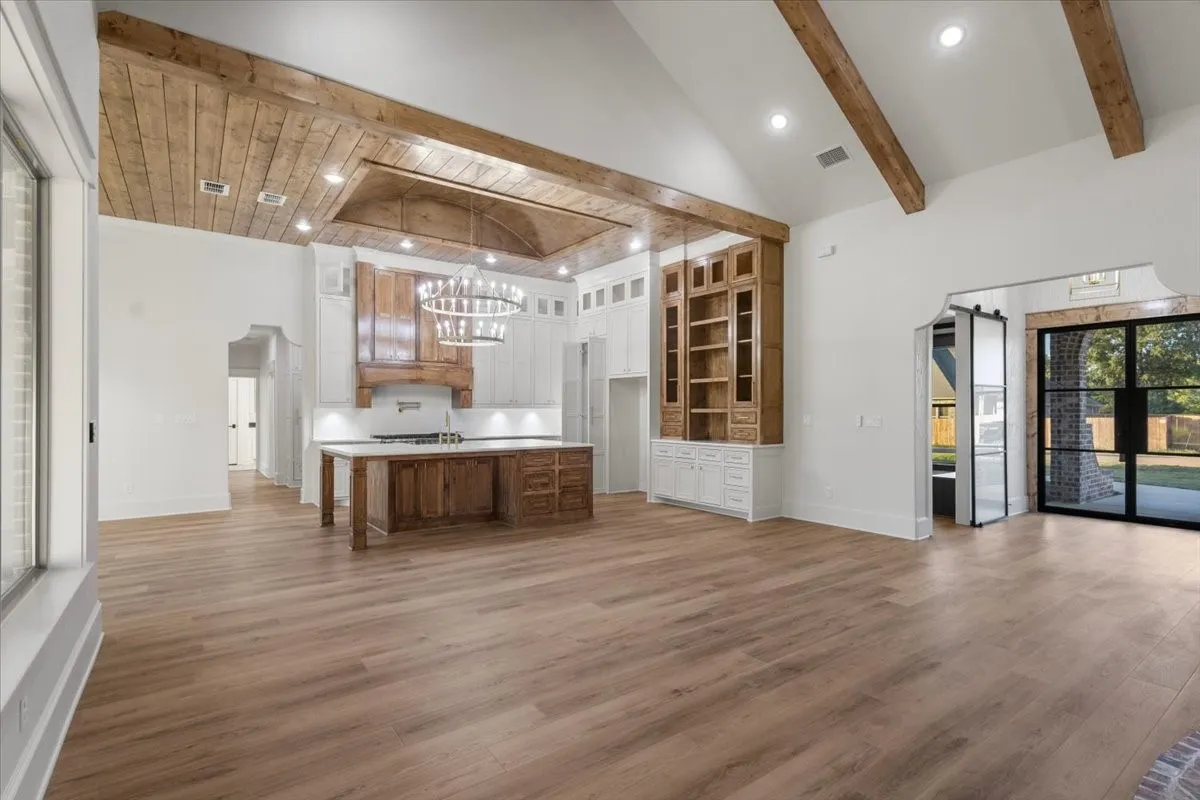 Vaulted ceiling with exposed wood beams, wood-finish flooring, built-in cabinetry with shelving, recessed lighting, and a kitchen island with built-in storage