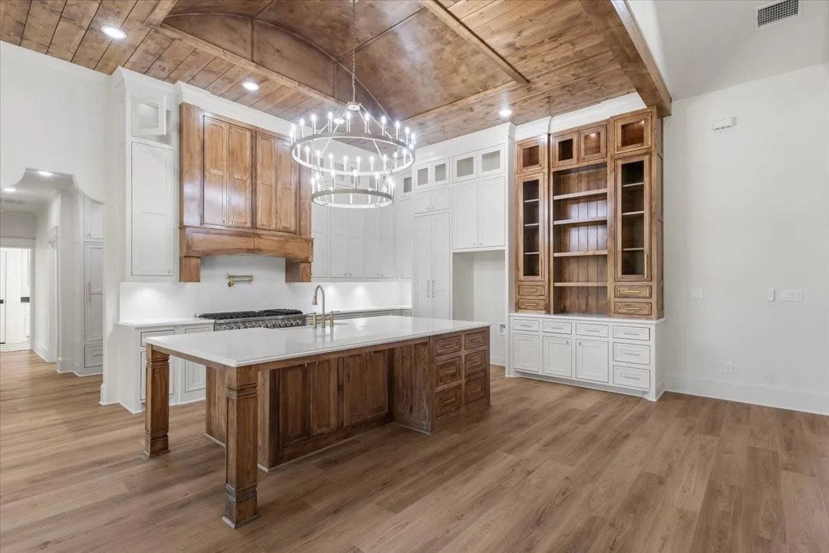 Vaulted wood-paneled ceiling with recessed lighting, large kitchen island with a light-toned countertop, wood-finish flooring, wood cabinetry, and a built-in shelving unit