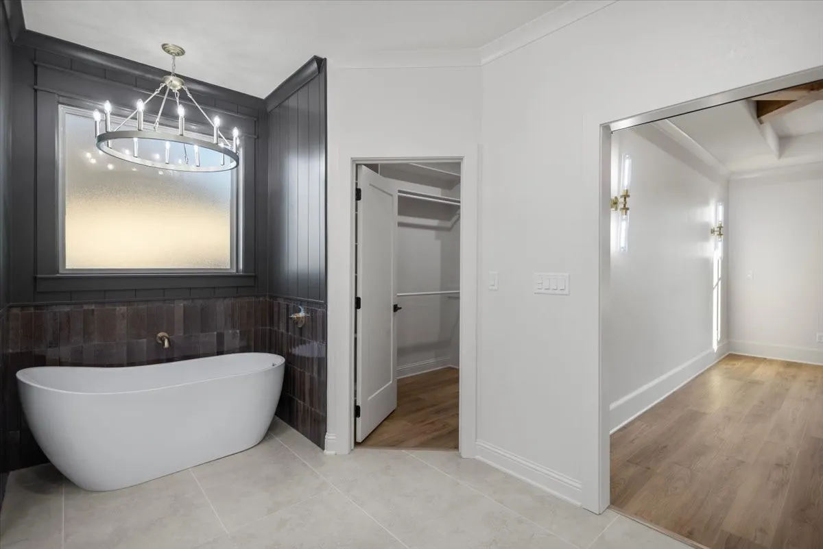 Freestanding bathtub with a bronze-finish faucet, dark wood wall paneling, and a contemporary chandelier
