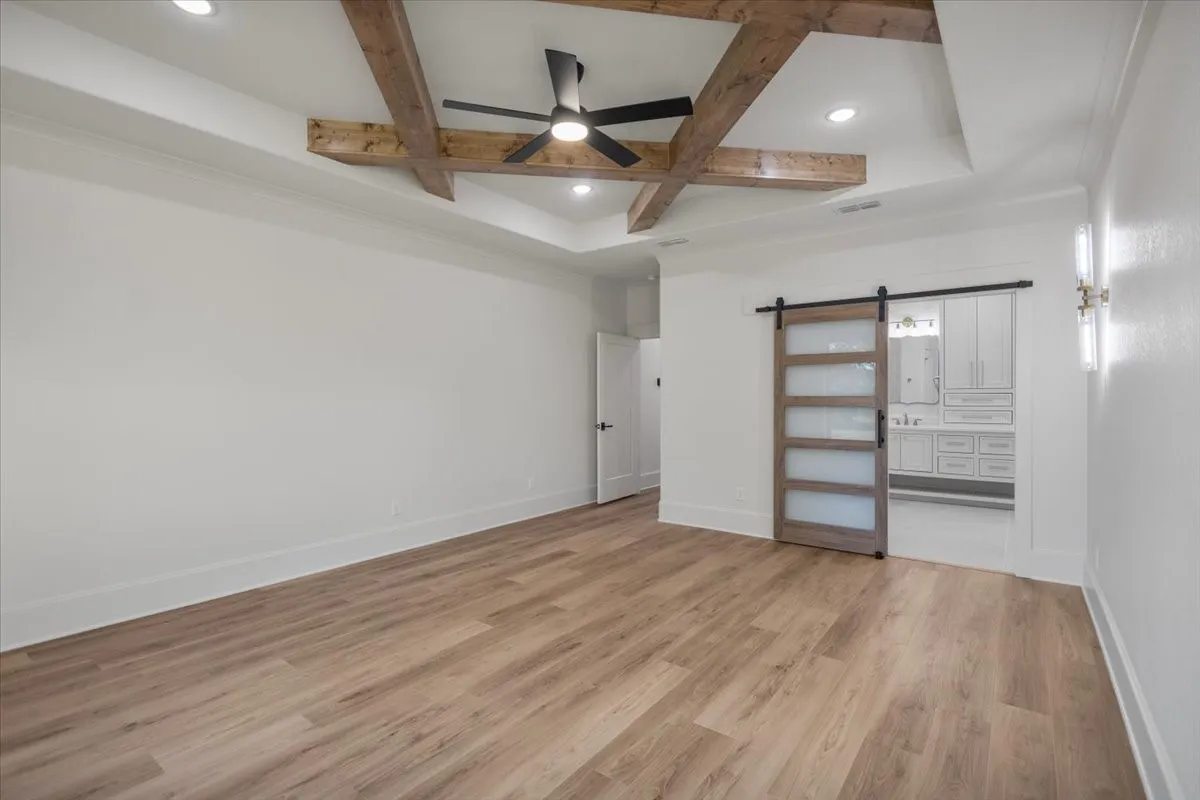 Wood-finish flooring, tray ceiling with wood beams, recessed lighting, and a barn door with frosted glass panels