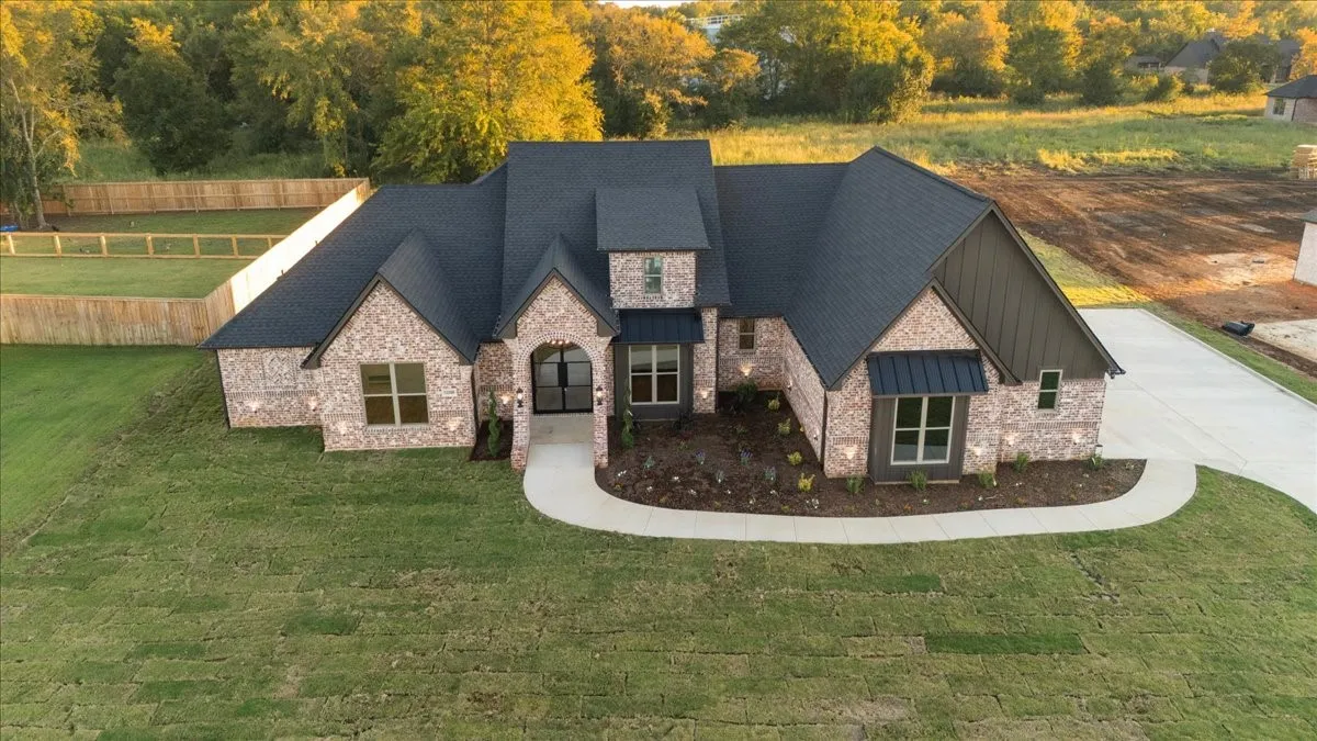 Brick and vertical siding exterior with a dark shingle roof, arched entryway, and a concrete driveway