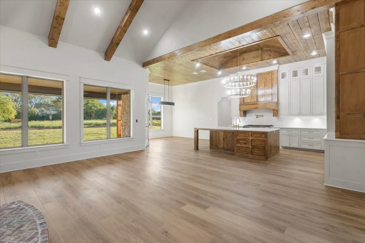 Vaulted ceiling with exposed wood beams, wood-finish flooring, recessed lighting, kitchen island with wood cabinetry, and white kitchen cabinetry