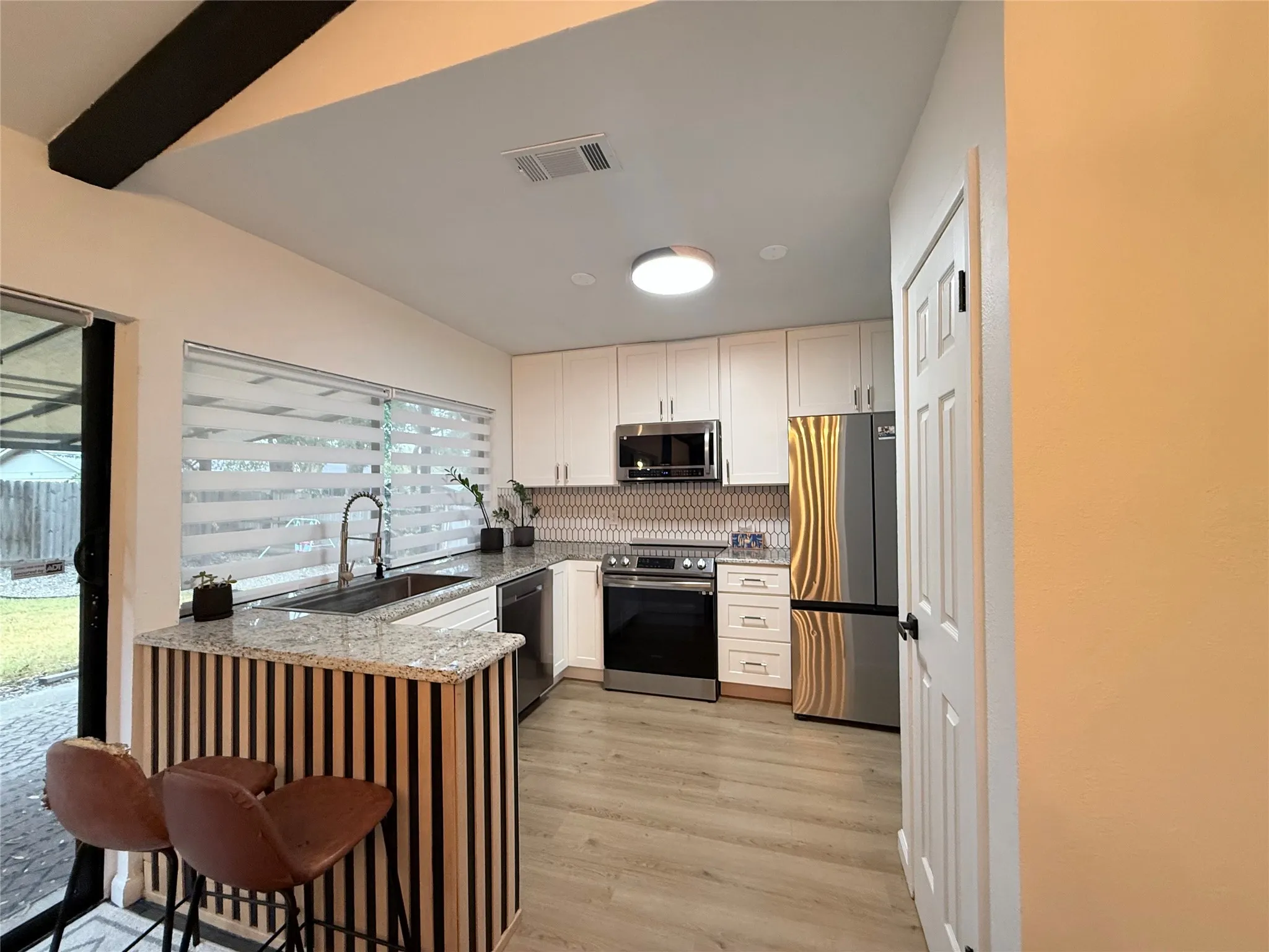 Kitchen featuring white cabinetry, stainless steel appliances, granite countertops, a tiled backsplash, and wood-finish flooring