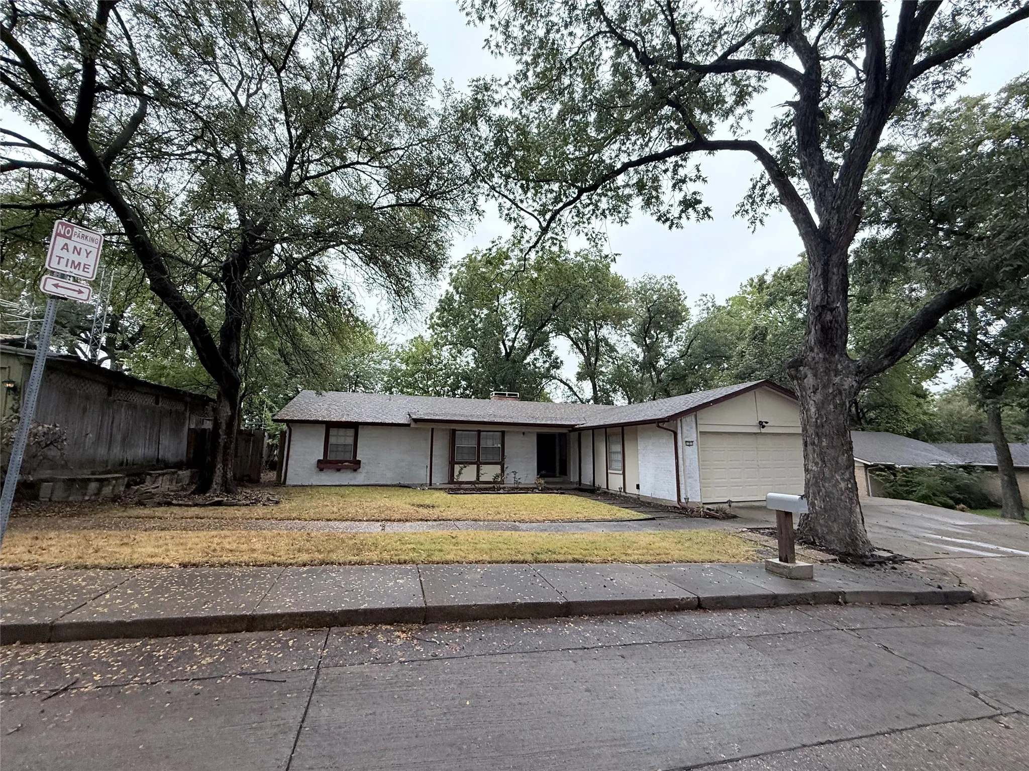 Ranch-style residence featuring a single-car garage, multiple mature trees, and a front yard area