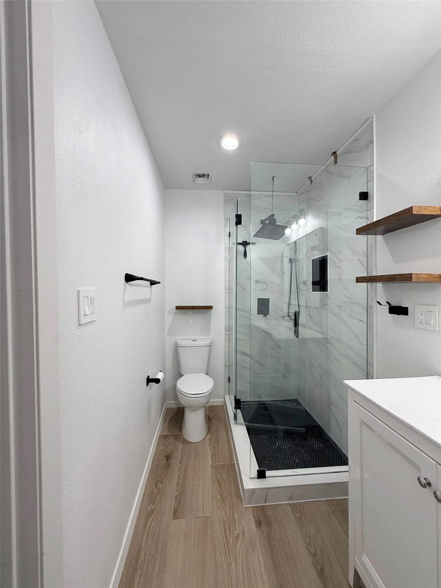 Walk-in shower with clear glass enclosure, marble-style wall tile, and black fixture finishes