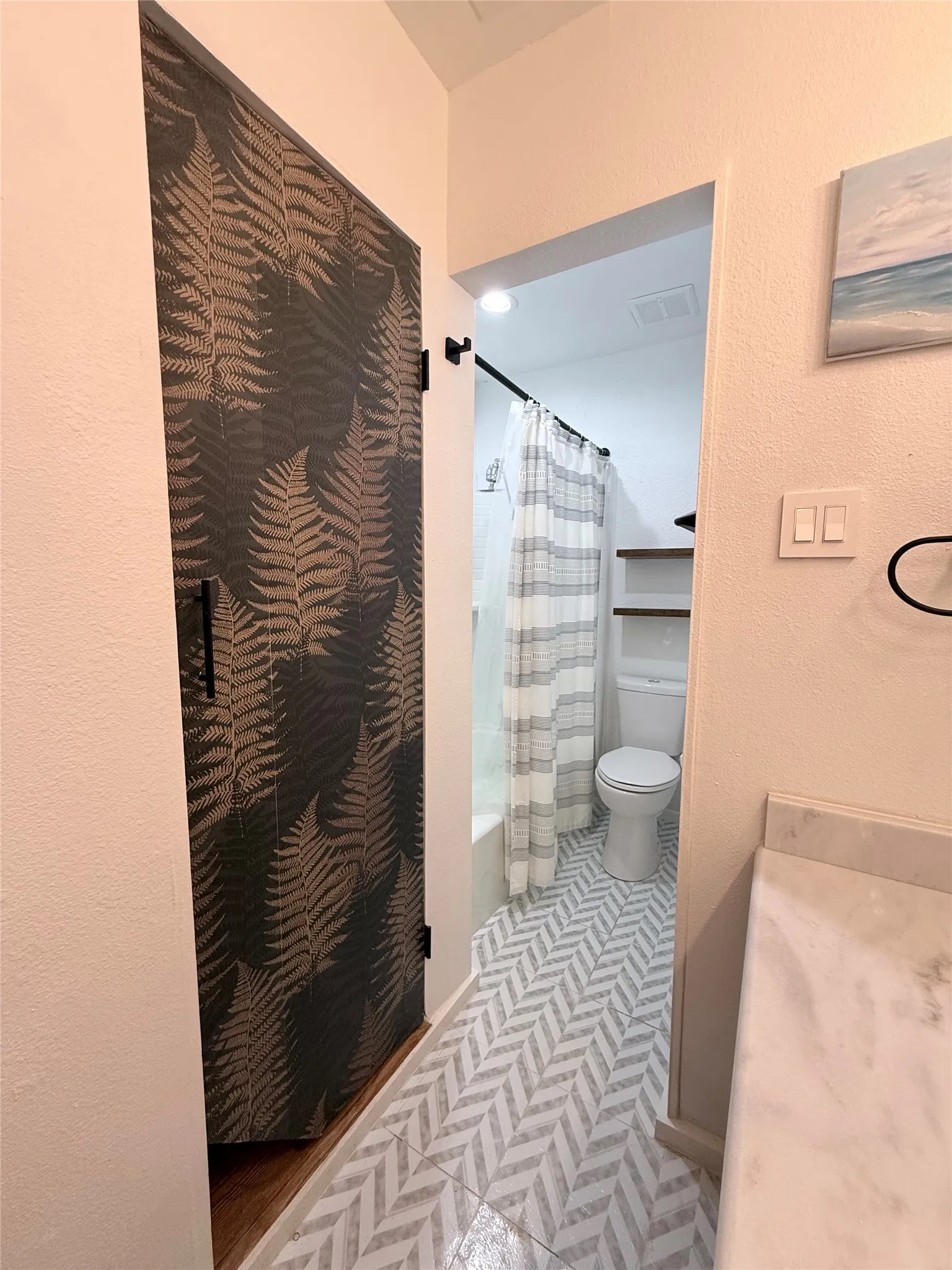 Barn door with fern-patterned finish, herringbone tile flooring, built-in shelving, and a stone-finish countertop
