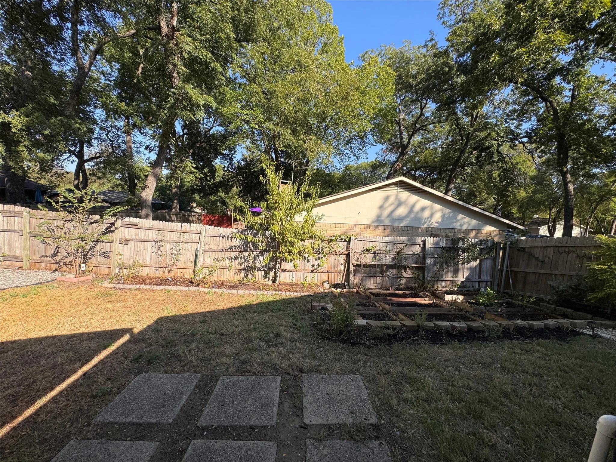 Private backyard featuring a wood privacy fence, concrete stepping stones, and a raised garden bed