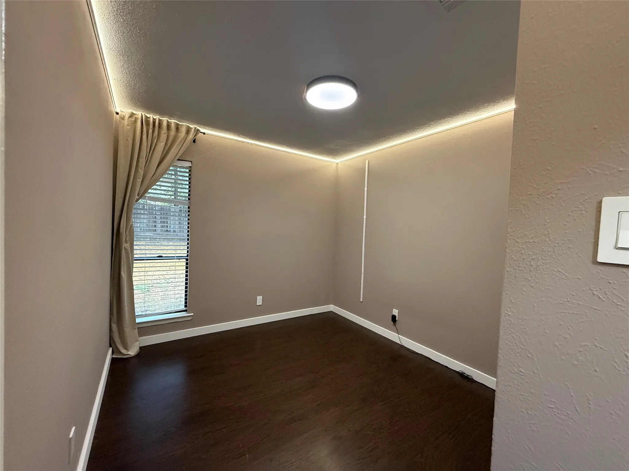 Wood-finish flooring, recessed ceiling lighting, light-colored wall paint, white baseboards, and window with blinds