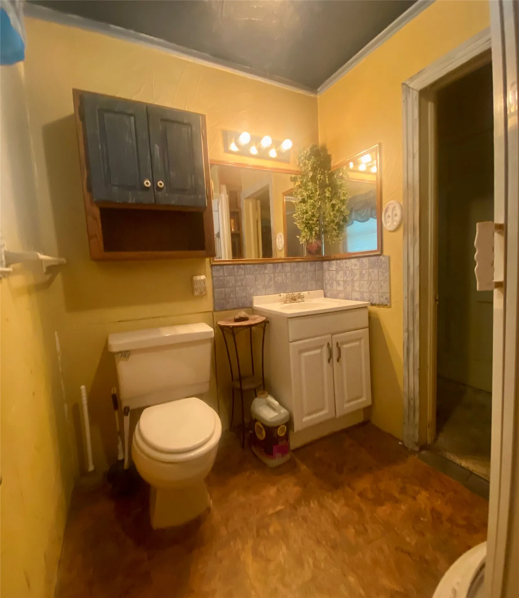 Bathroom featuring a white vanity with integrated sink, a wall-mounted mirror with overhead lighting, a toilet, and wood-finish flooring