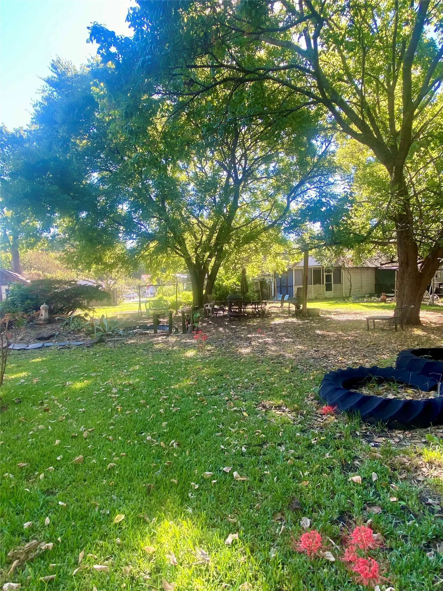Expansive backyard featuring mature trees, a manicured lawn, and vibrant red flowering plants