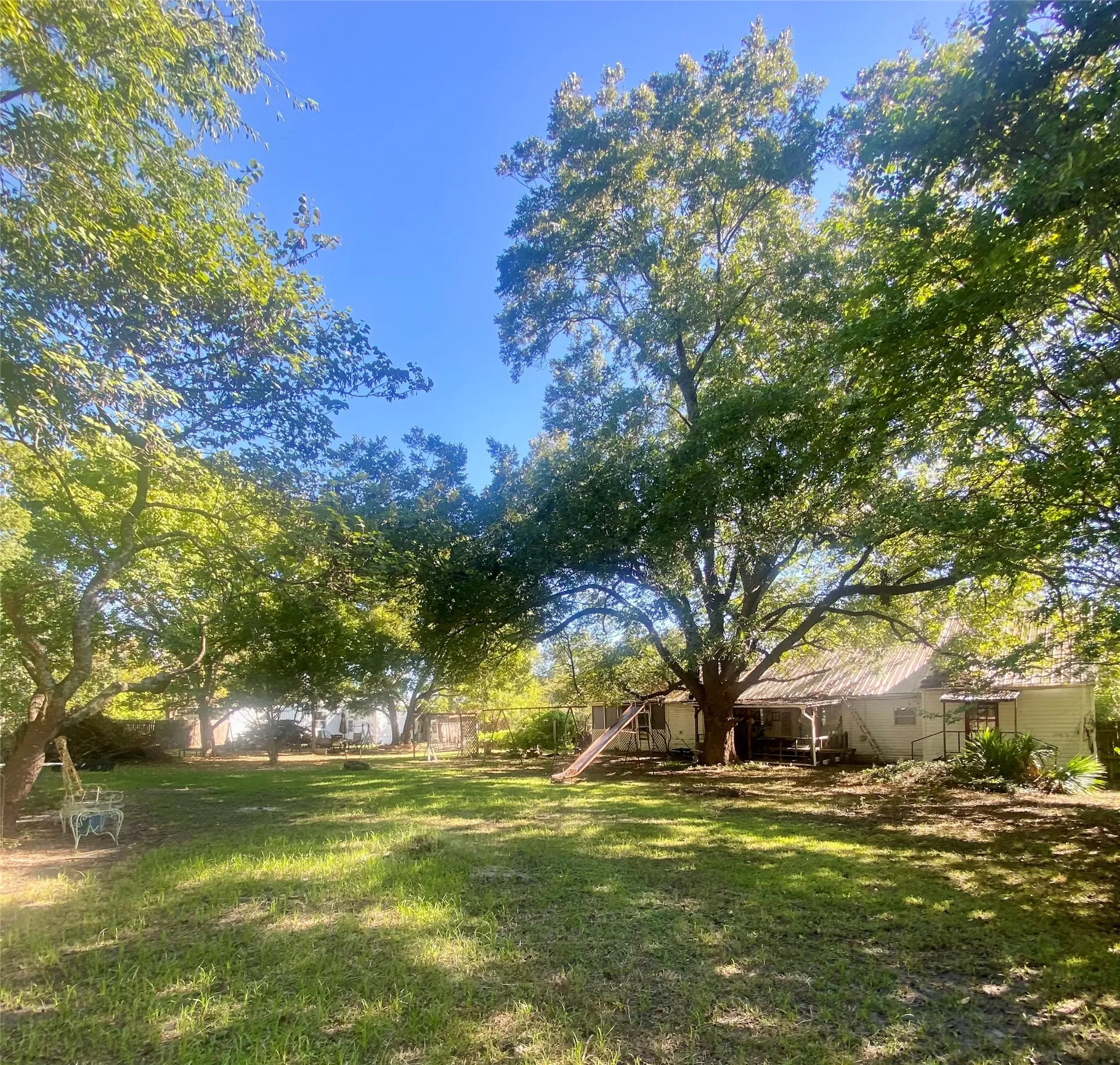 Expansive yard with mature trees providing ample shade and a grass lawn