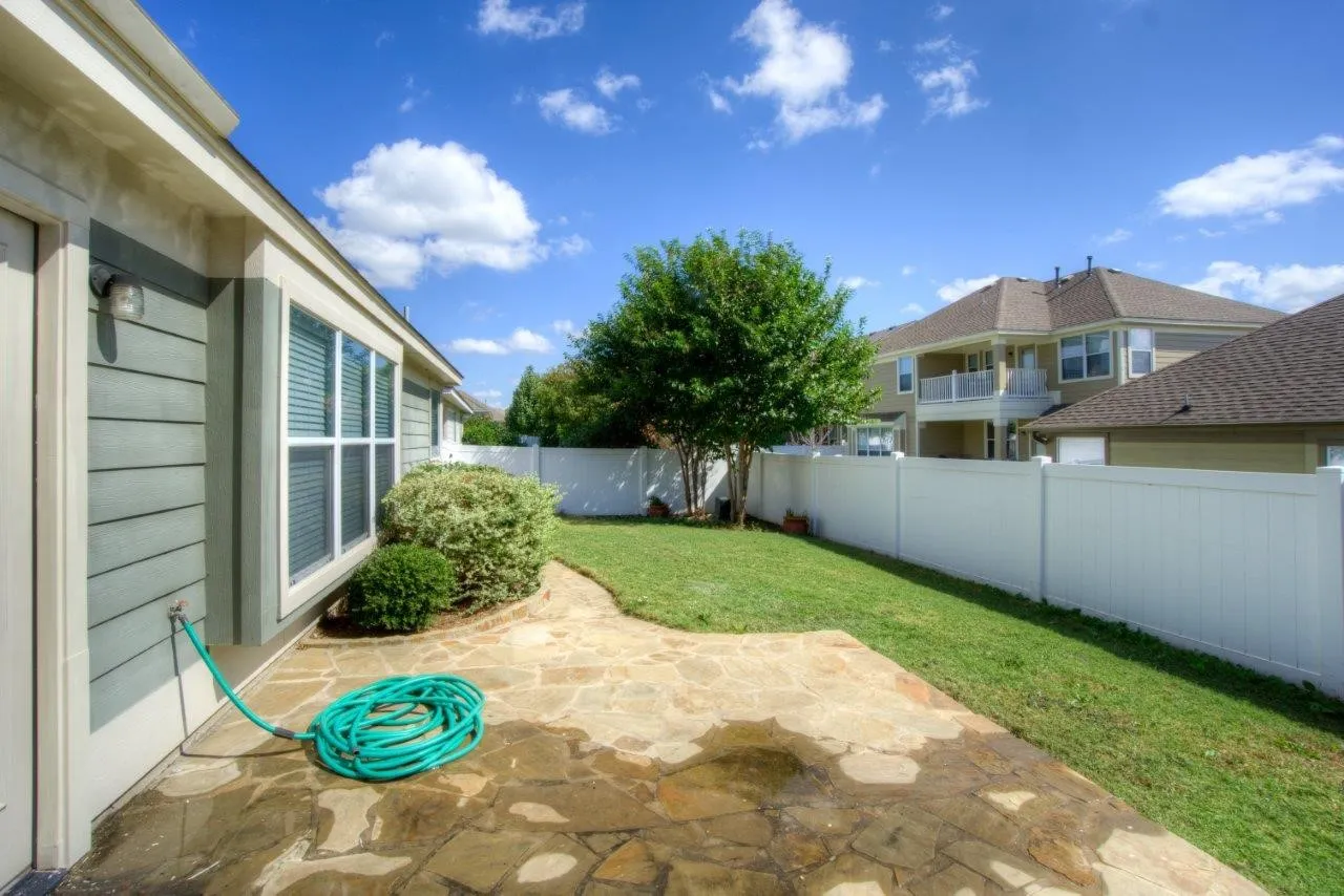 Expansive flagstone patio area with a grass lawn, mature tree, and privacy fencing
