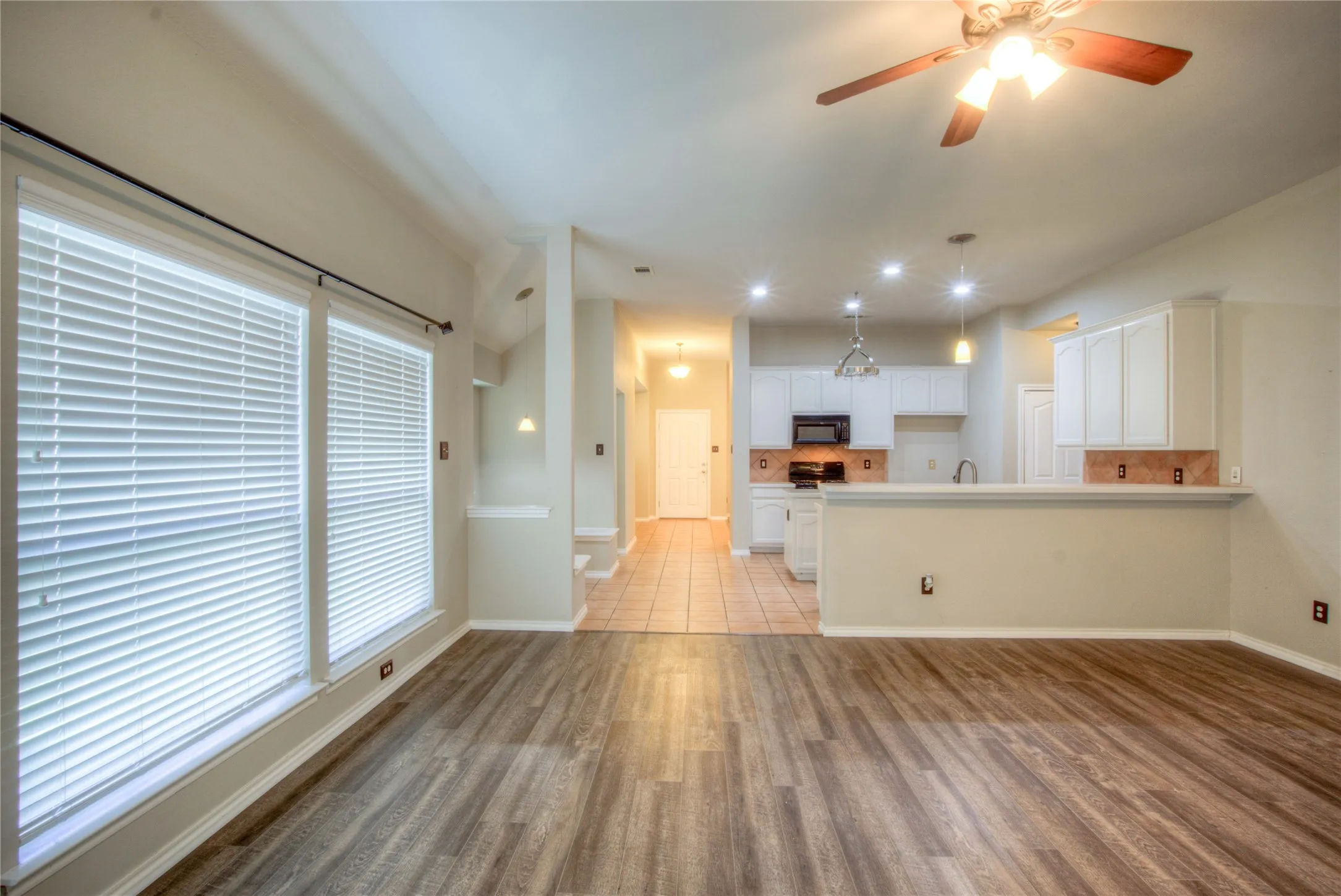 Wood-finish flooring, recessed lighting, ceiling fan, white cabinetry, and a kitchen pass-through