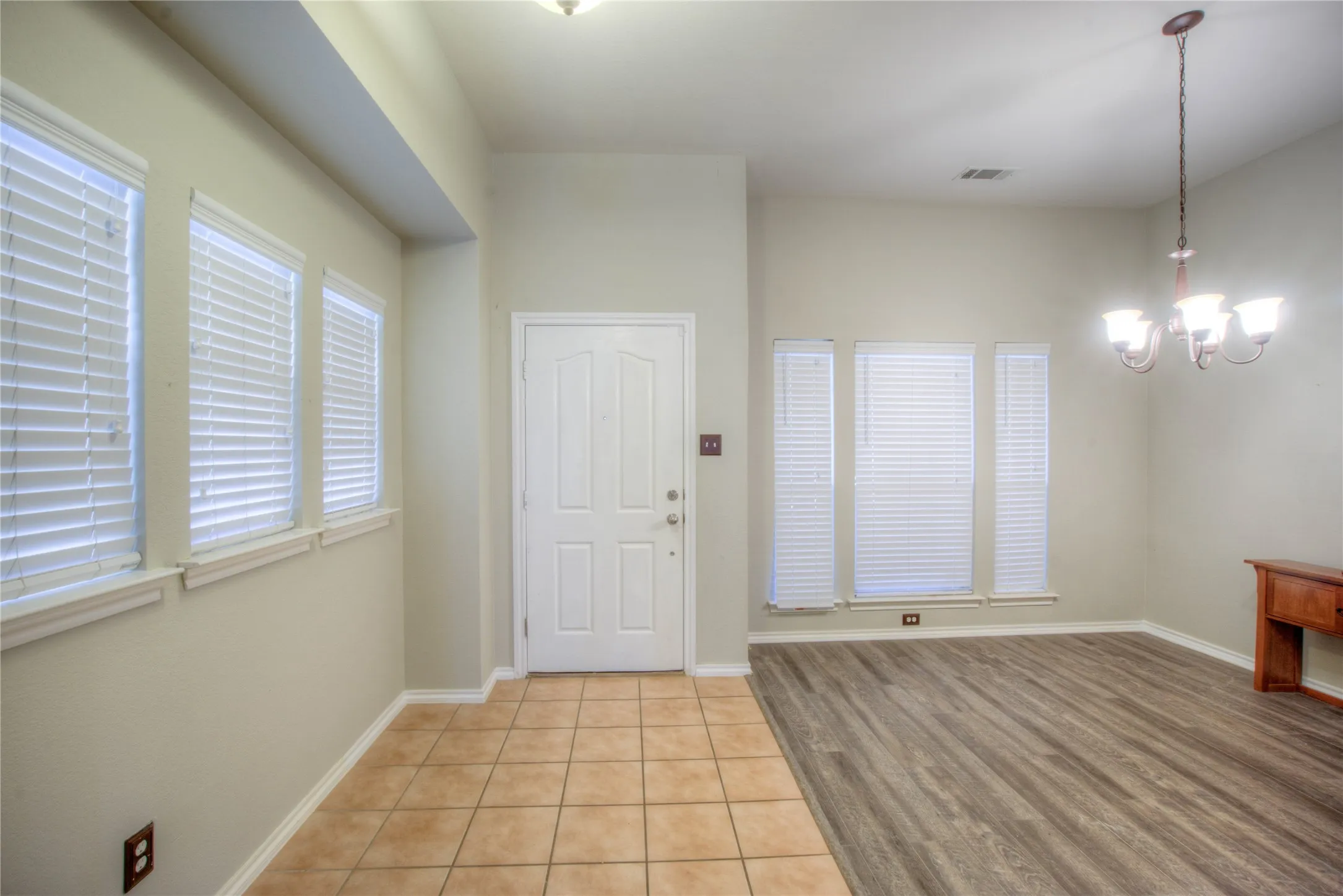 Entryway featuring tile flooring, a paneled door, and adjacent room with wood-finish flooring, a multi-light chandelier, and multiple windows