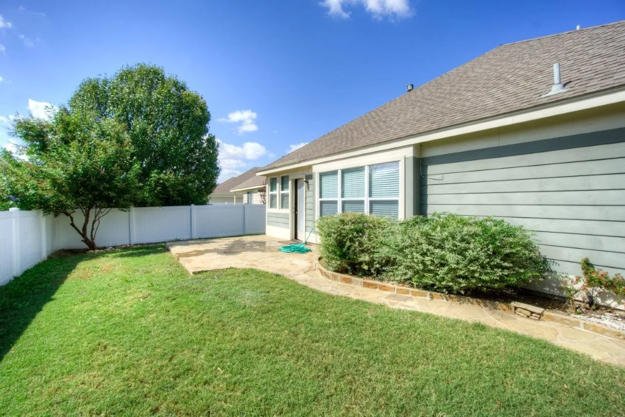 Private fenced backyard featuring a stone patio, manicured lawn, and mature tree