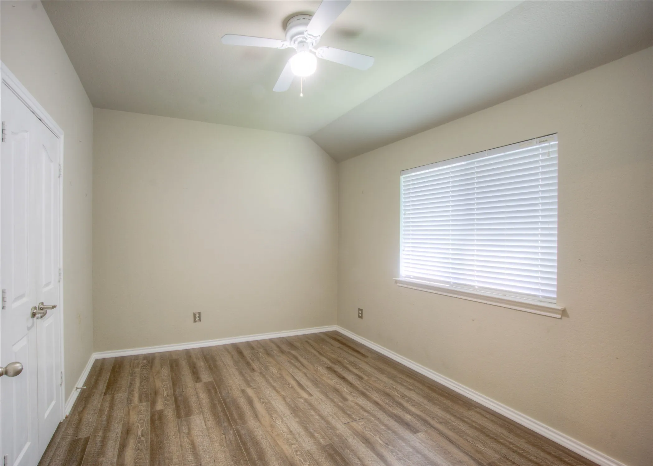 Wood-finish flooring, neutral wall tones, window with horizontal blinds, overhead ceiling fan with lighting, and white paneled doors