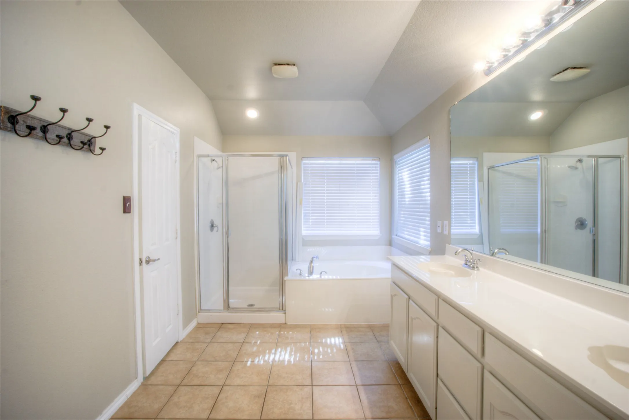 Dual vanity with integrated sinks, large mirror, recessed lighting, and a glass-enclosed shower