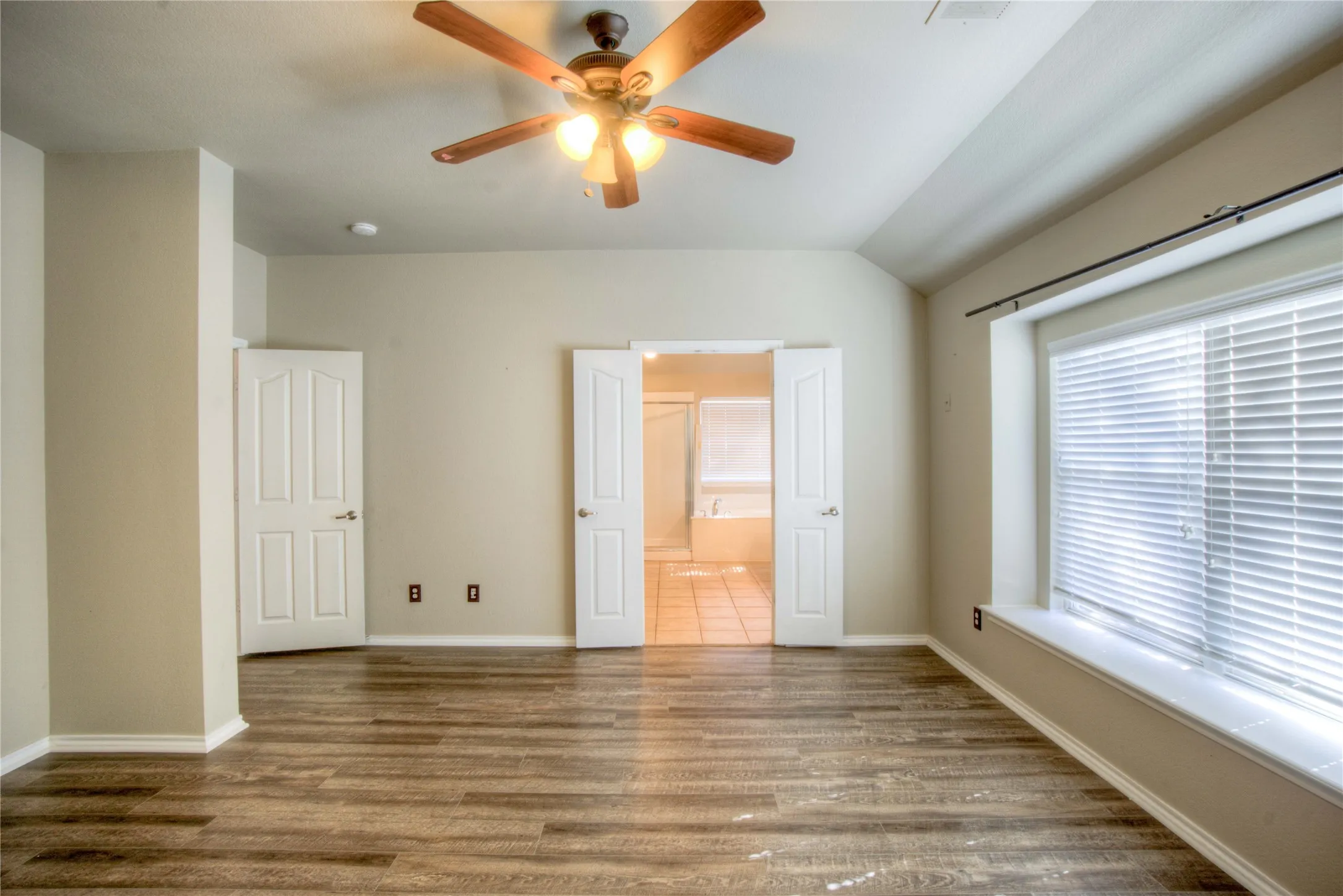 Vaulted ceiling with a ceiling fan, wood-finish flooring, and a wide window with blinds