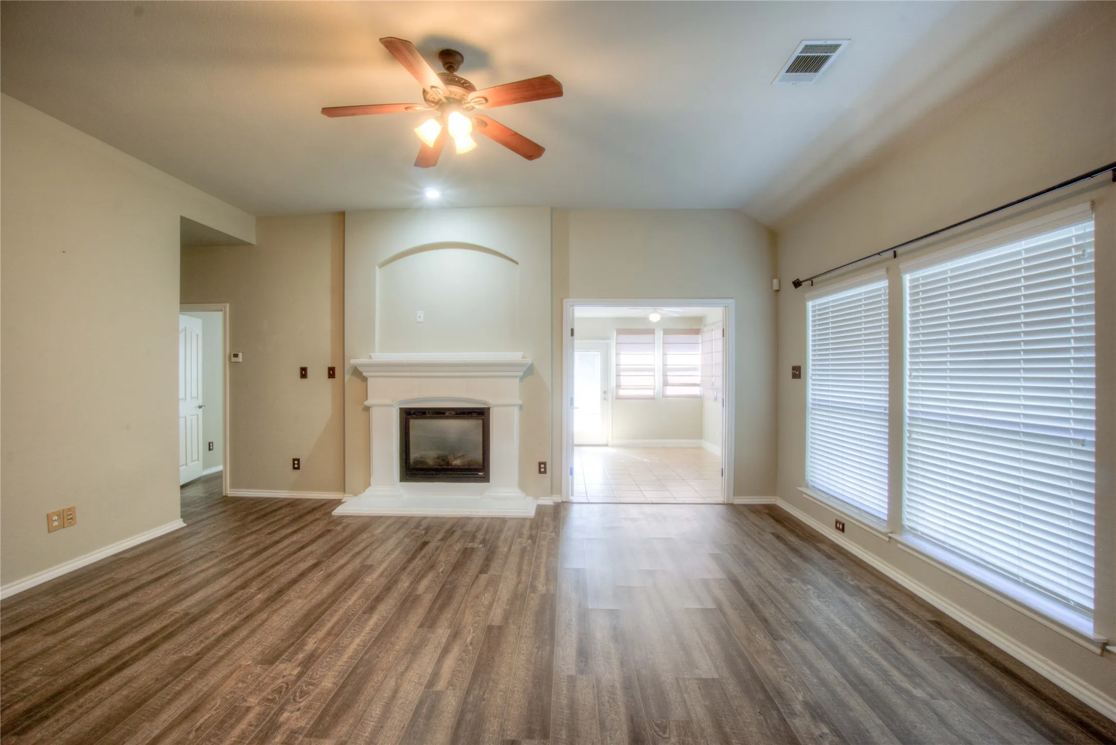 Wood-finish flooring throughout, ceiling fan with integrated lighting, built-in fireplace with mantel, recessed lighting, and multiple windows with blinds