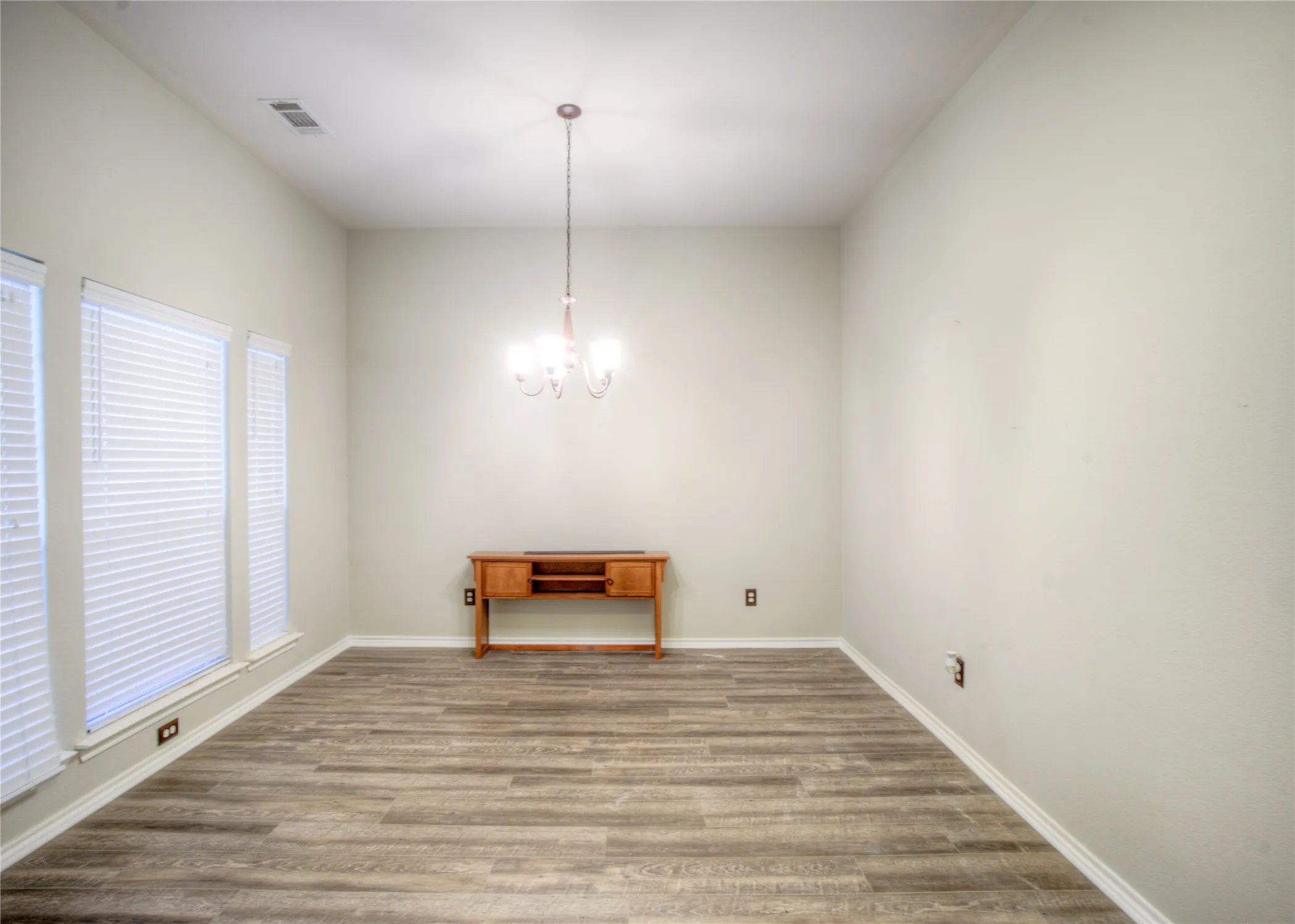 Wood-finish flooring, multiple windows with blinds, and a chandelier lighting fixture
