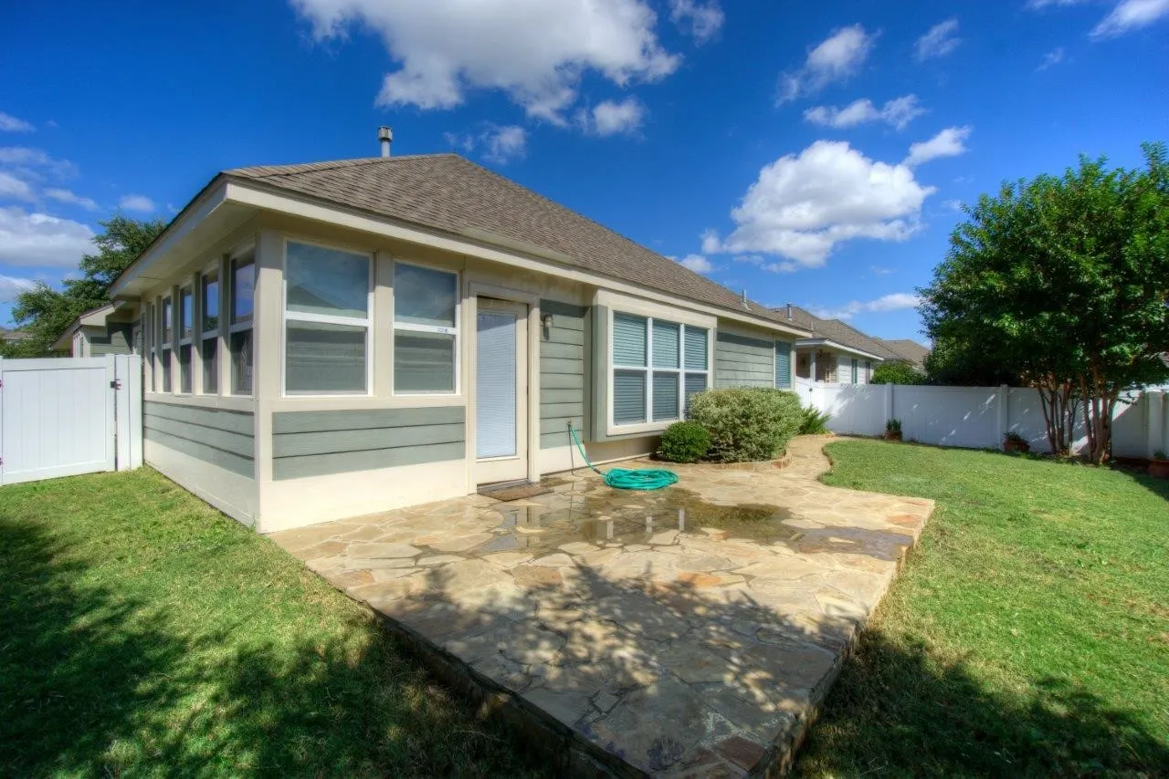 Exterior featuring light green siding, multiple windows, a stone patio, and a white fence