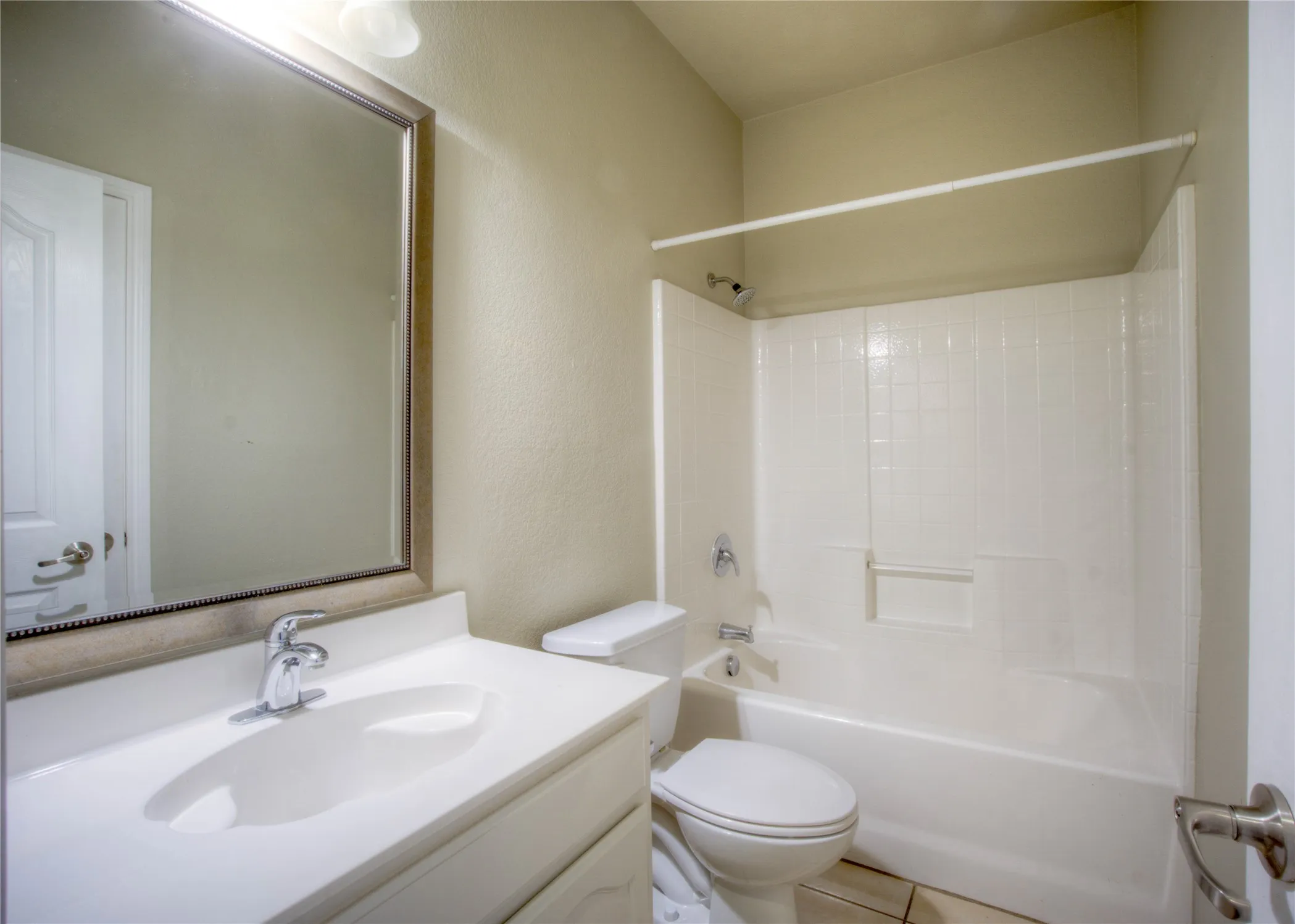 White vanity with integrated sink, chrome faucet, framed mirror, and a shower/tub combination with subway-style wall surround