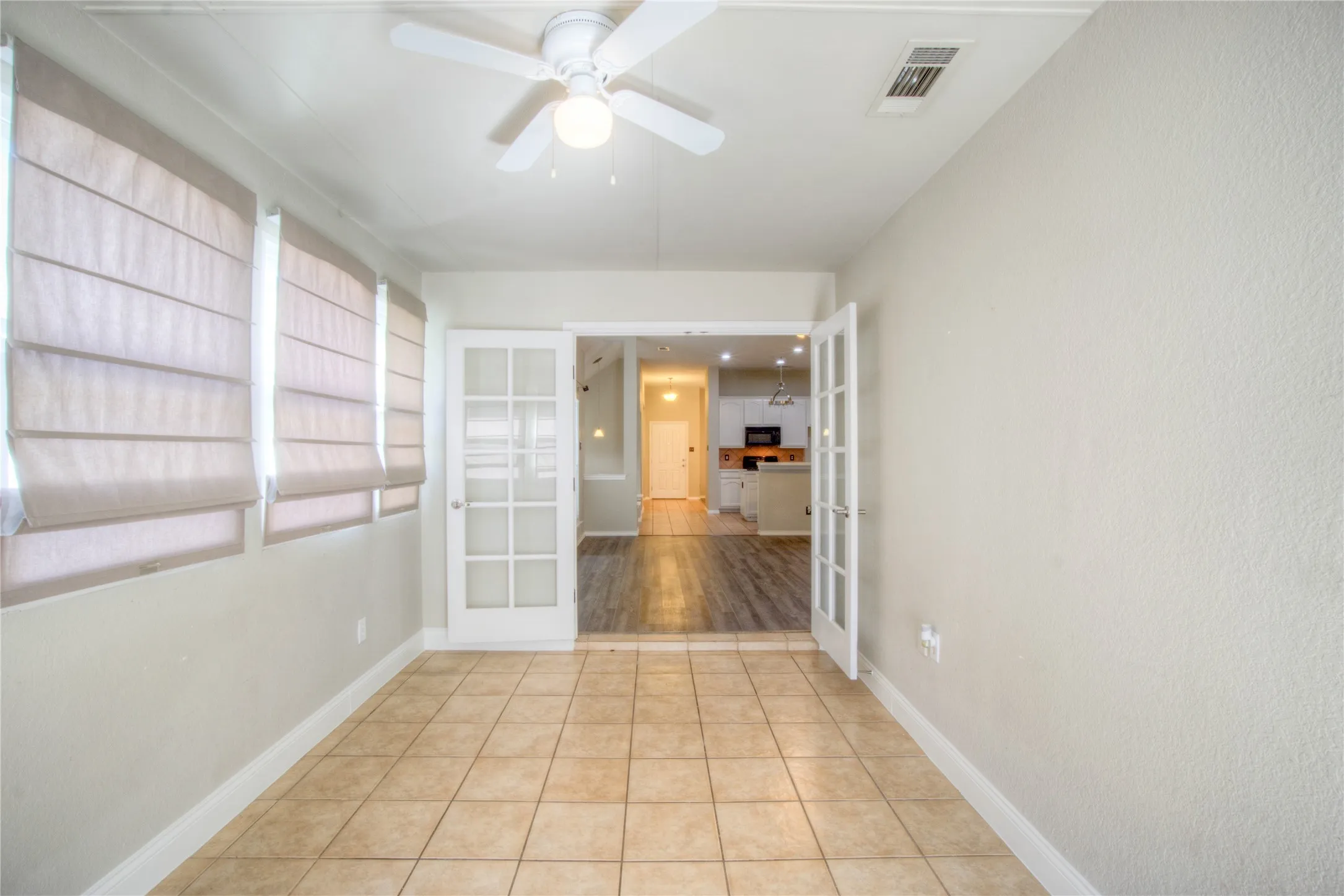 Room featuring tile flooring, a ceiling fan, and multiple windows with blinds