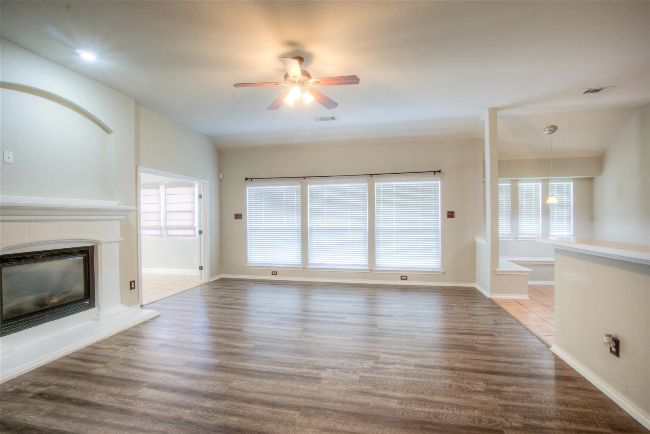 Wood-finish flooring throughout, white fireplace mantel, multiple windows with blinds, ceiling fan with integrated lighting, and recessed lighting