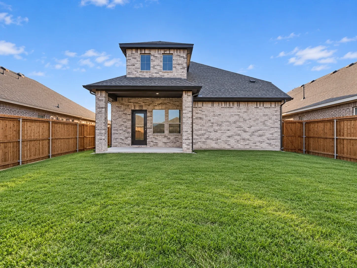 Expansive backyard featuring a manicured lawn, full privacy fencing, and a covered patio