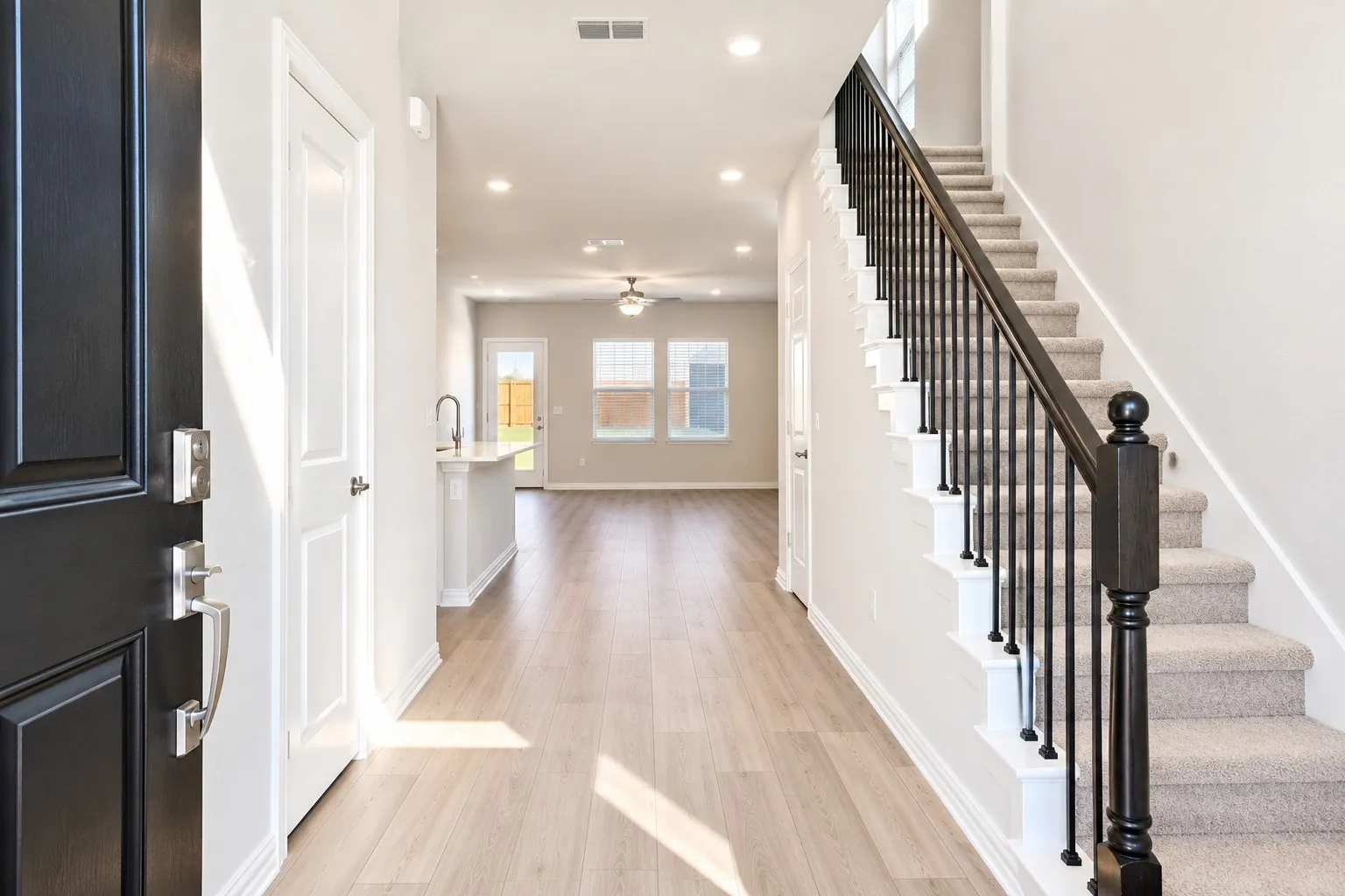 Wood-finish flooring, recessed lighting, carpeted staircase with dark wood newel post and black metal balusters, and a kitchen island with a single-basin sink