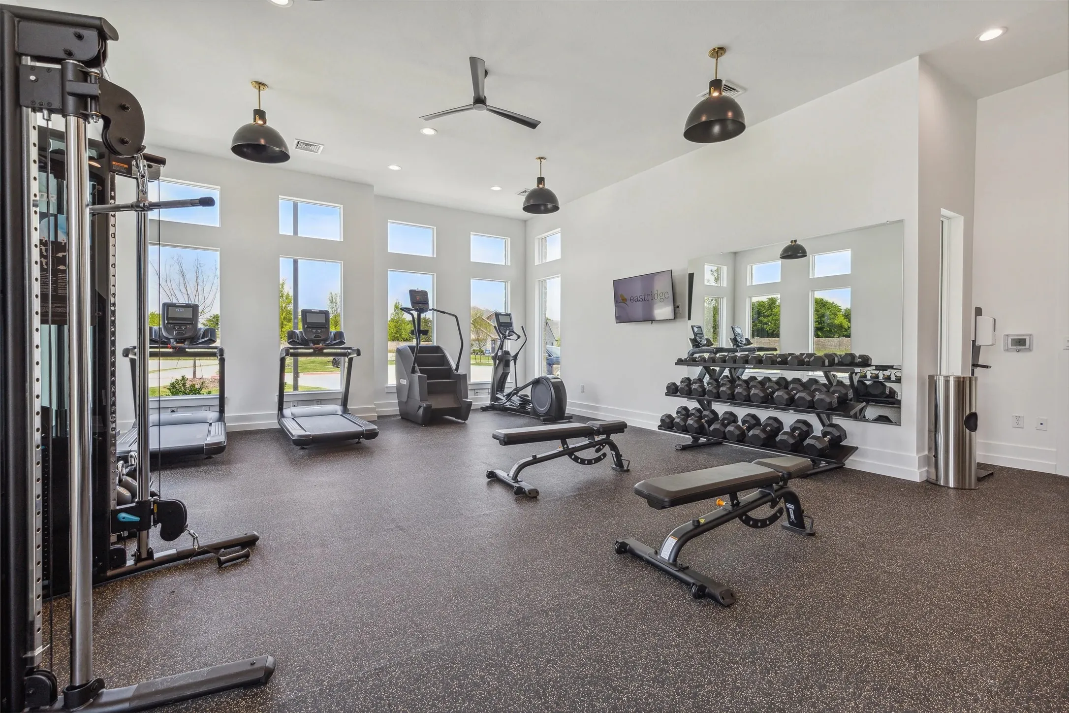 Fitness area with large wall-mounted mirror, multiple windows, ceiling fan, and recessed lighting