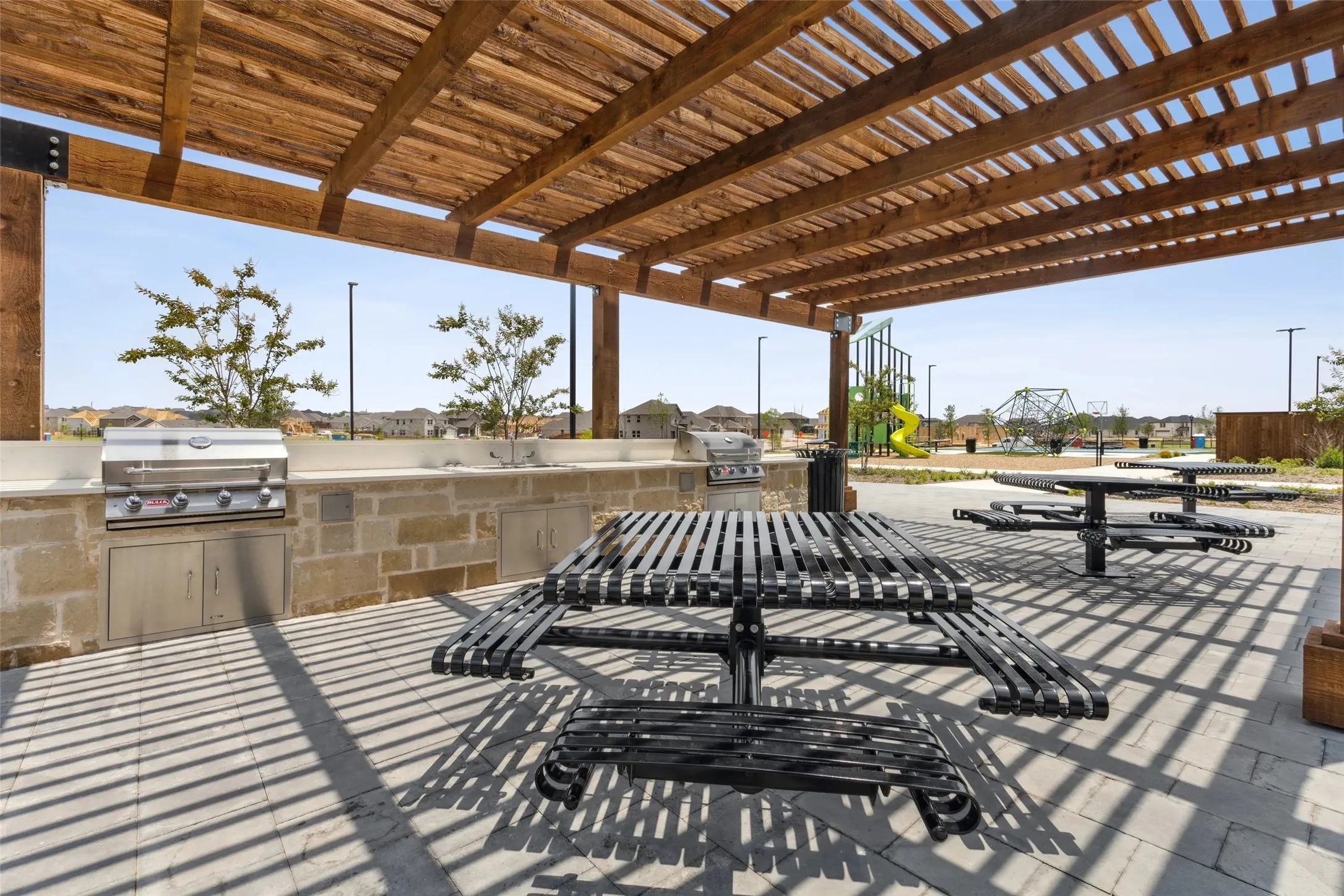 Expansive outdoor patio with a wooden pergola, built-in stone outdoor kitchen, integrated stainless steel grill, and paver flooring