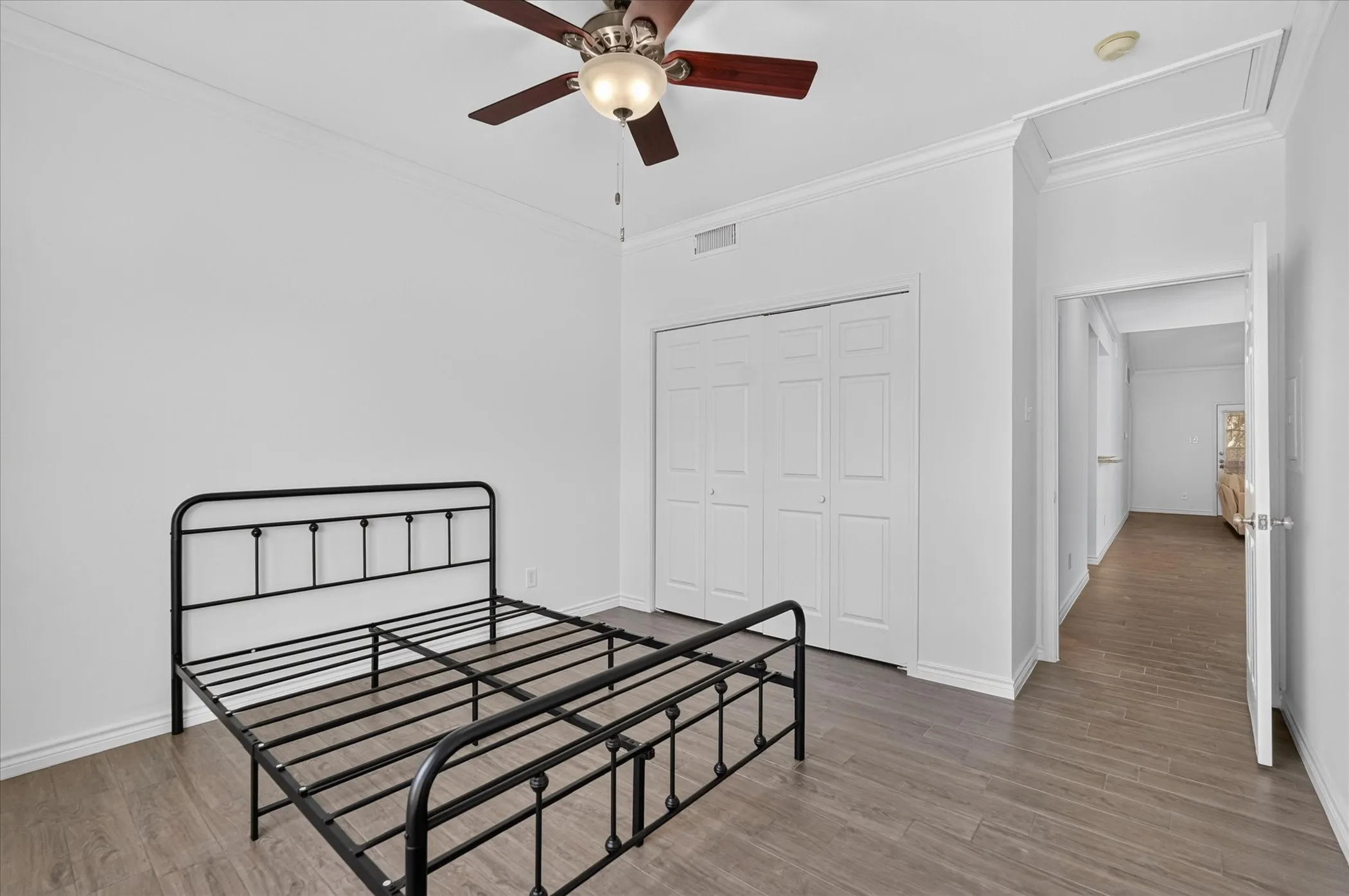 Wood-finish flooring, ceiling fan with integrated lighting, bi-fold closet doors, and crown molding