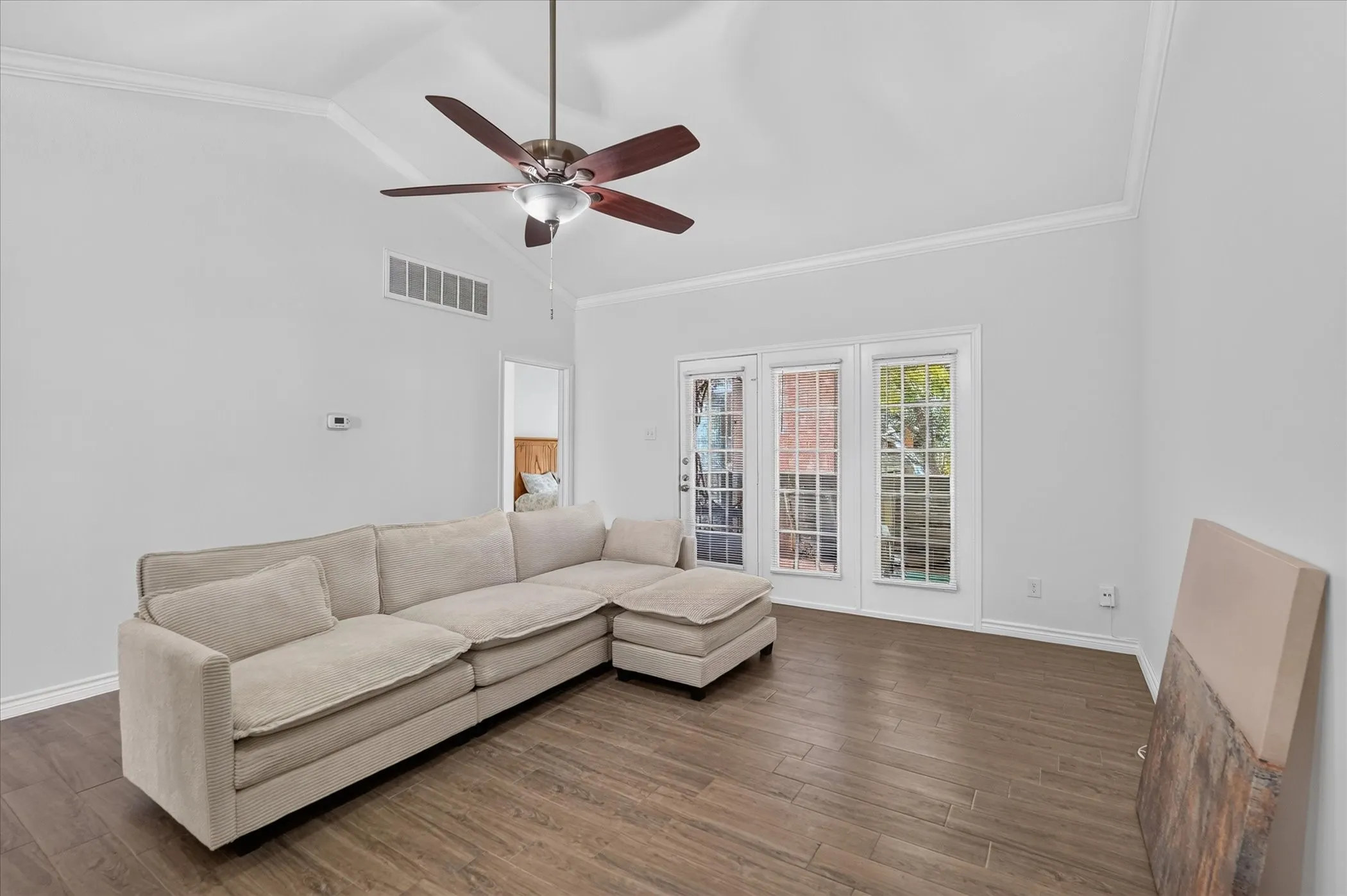 Vaulted ceiling with a ceiling fan, crown molding, wood-finish flooring, and multiple window panels