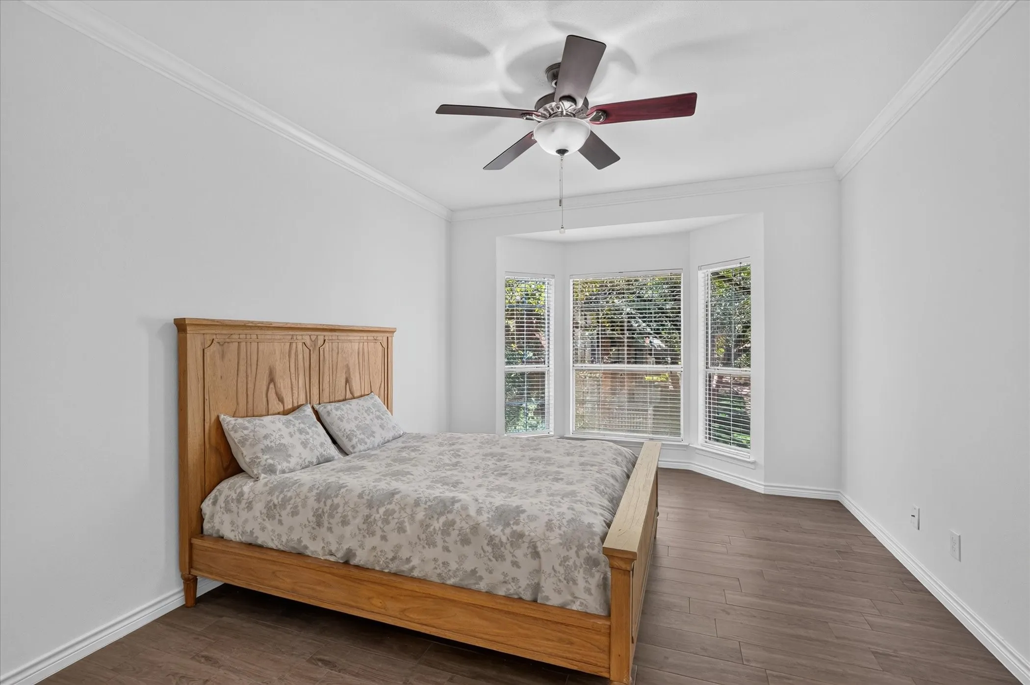 Bay window with multiple panes, wood-finish flooring, ceiling fan, and crown molding