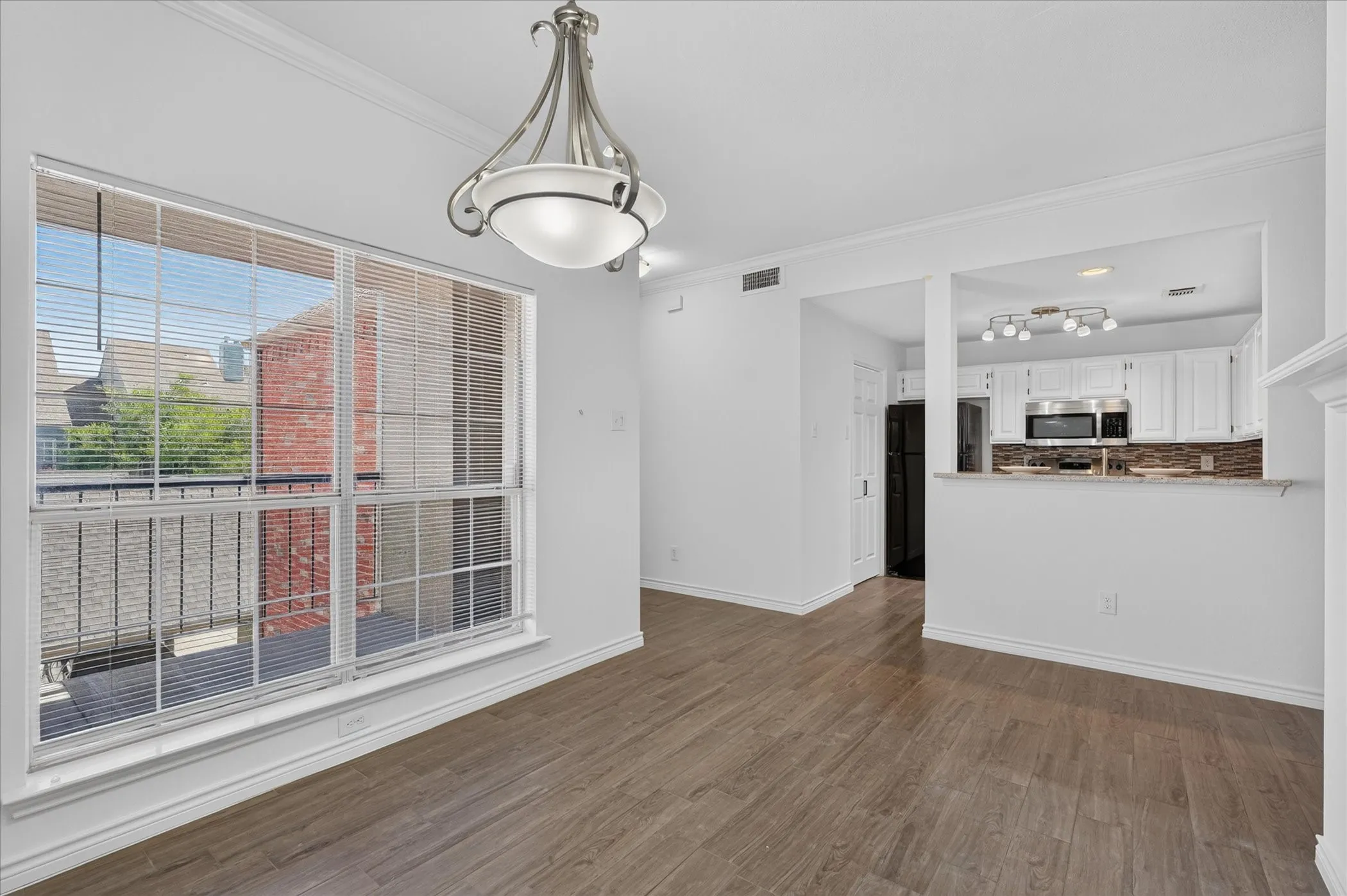 Spacious room featuring wood-finish flooring, a large window with blinds, and a decorative ceiling light fixture