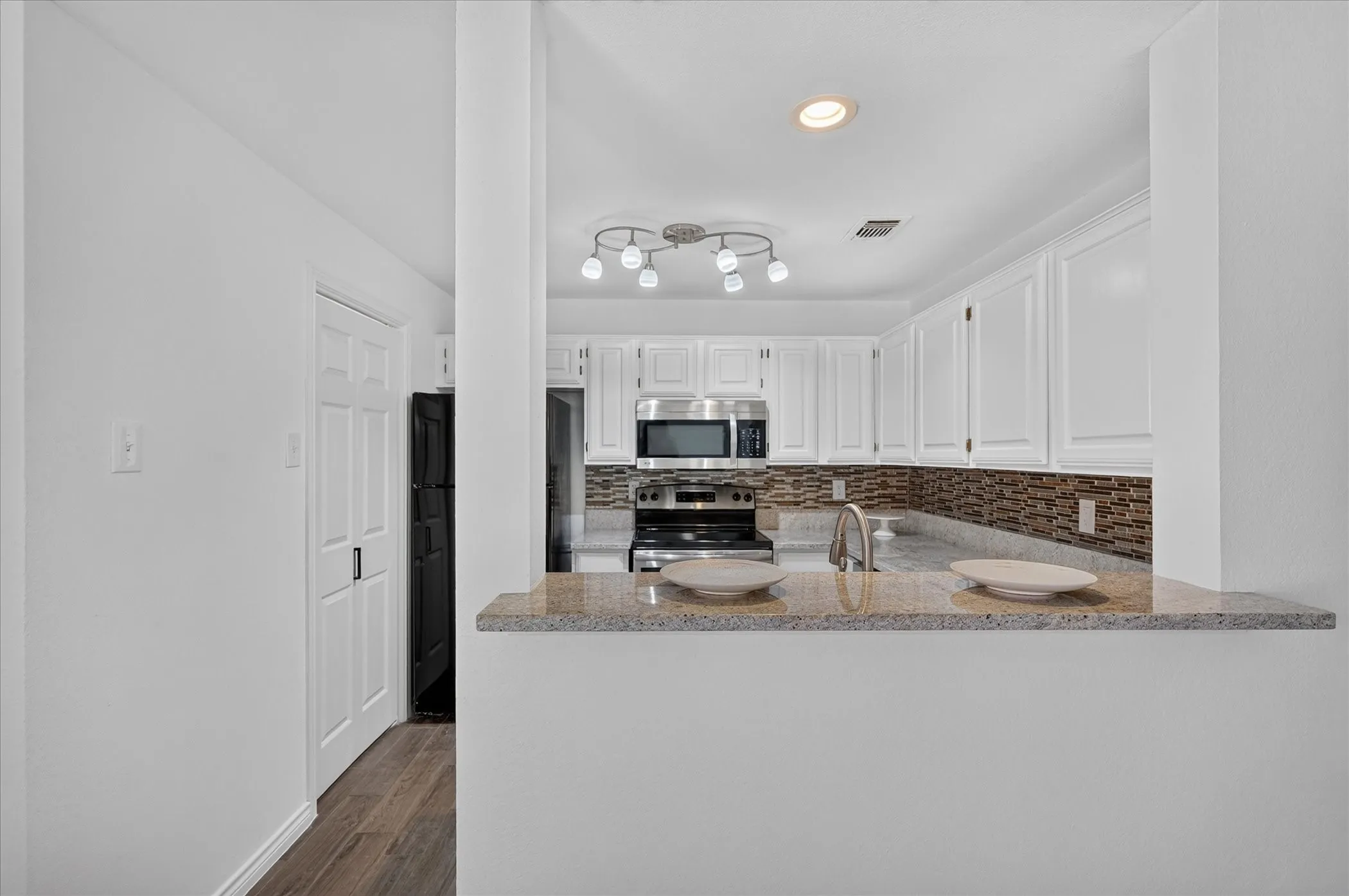 White cabinetry, granite countertop, stainless steel appliances, patterned tile backsplash, and wood-finish flooring