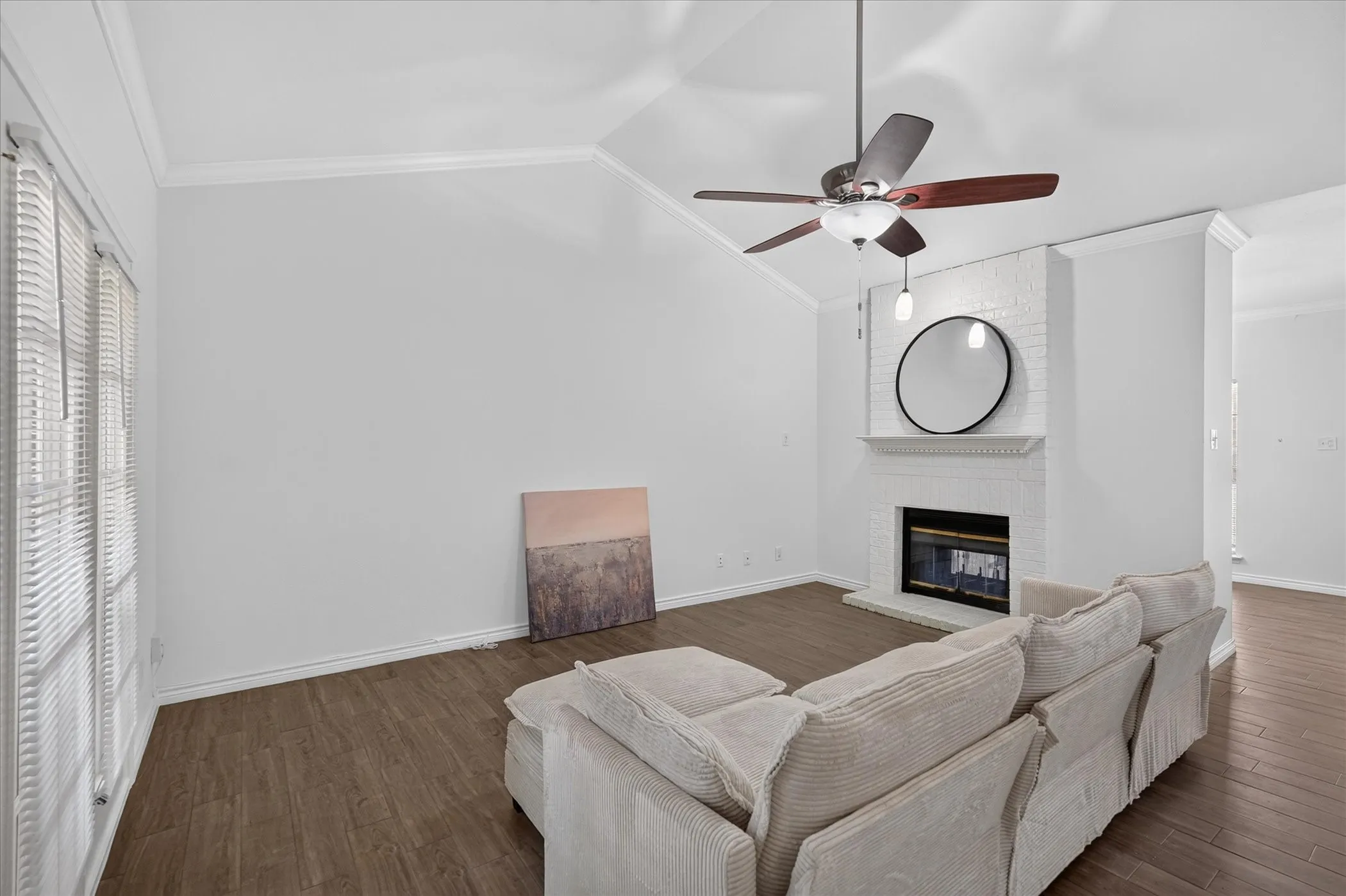 Vaulted ceiling with a ceiling fan, white painted brick fireplace with hearth, and wood-finish flooring