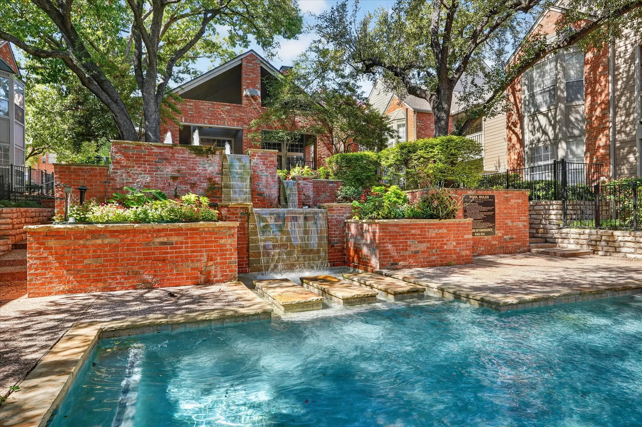 Outdoor swimming pool with stone coping and a multi-tiered brick water feature with integrated planters