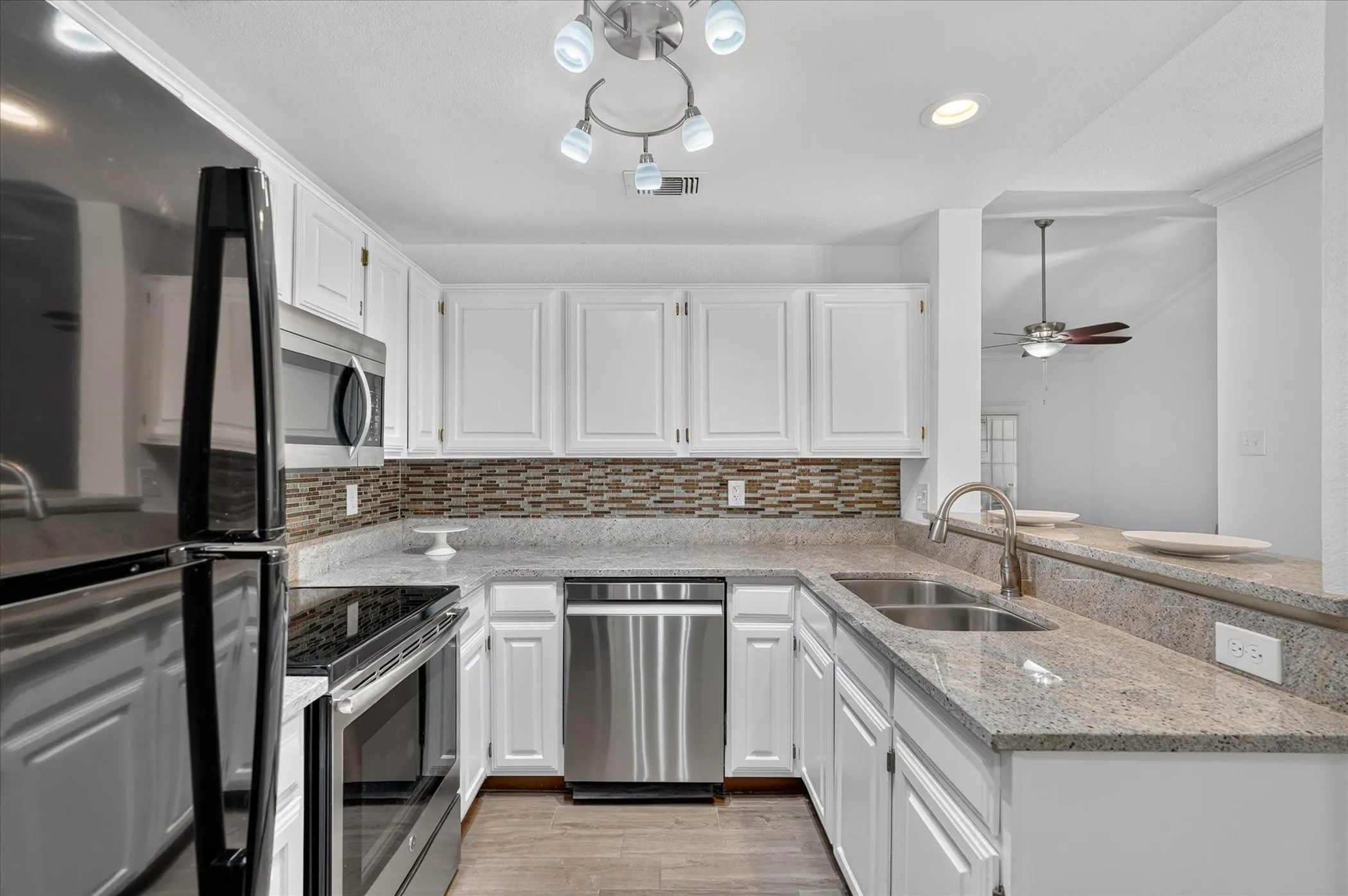 Kitchen featuring white cabinetry, stone countertops, stainless steel appliances, a tiled backsplash, and wood-finish flooring
