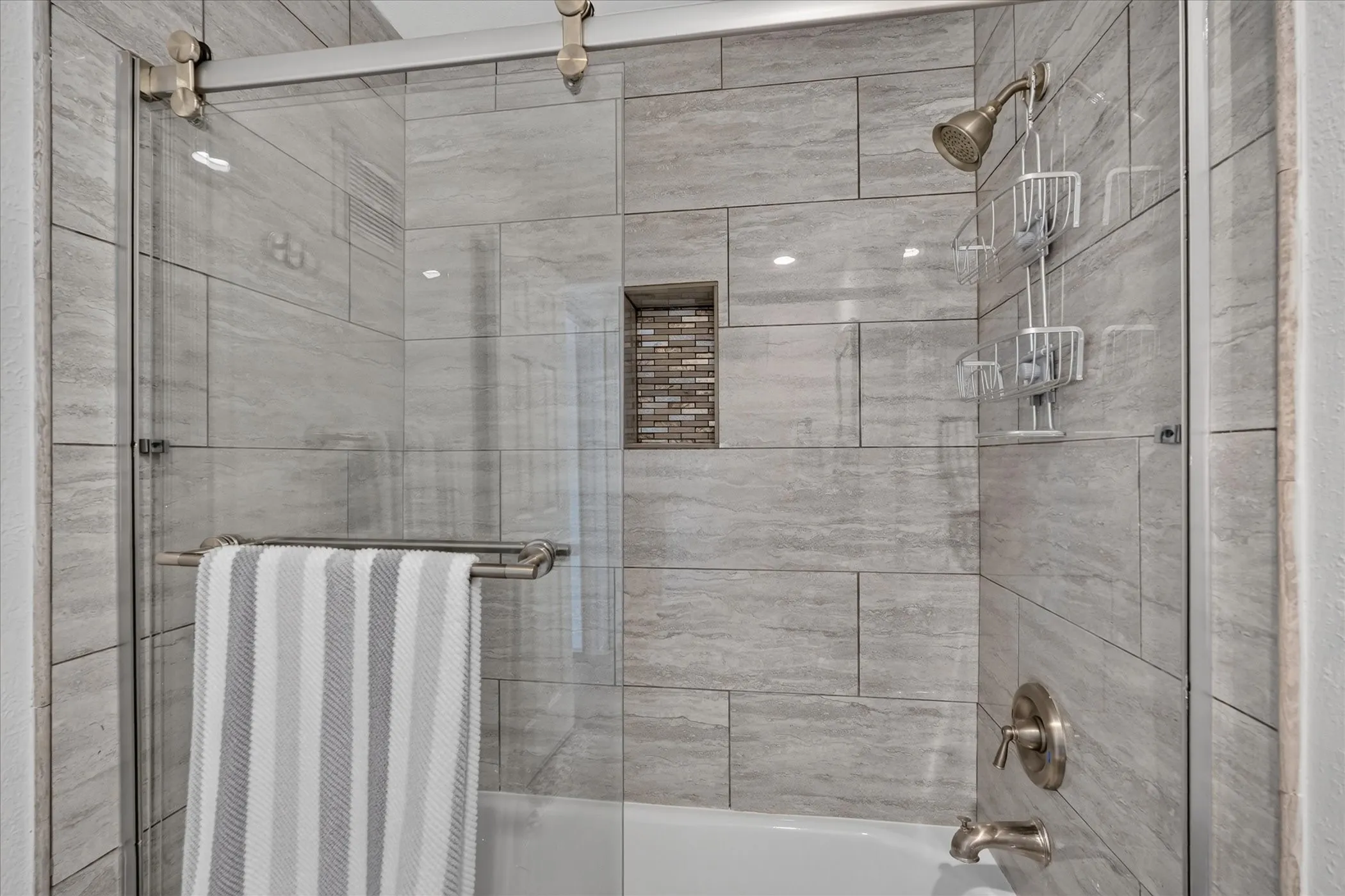 Bathtub with light gray subway tile surround and integrated tiled niche