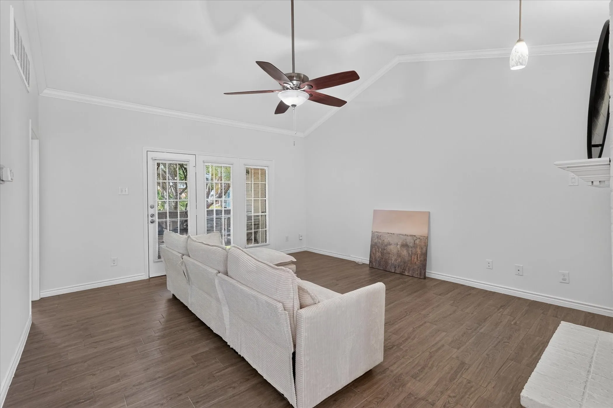Vaulted ceiling with crown molding, wood-finish flooring, ceiling fan, and two French doors